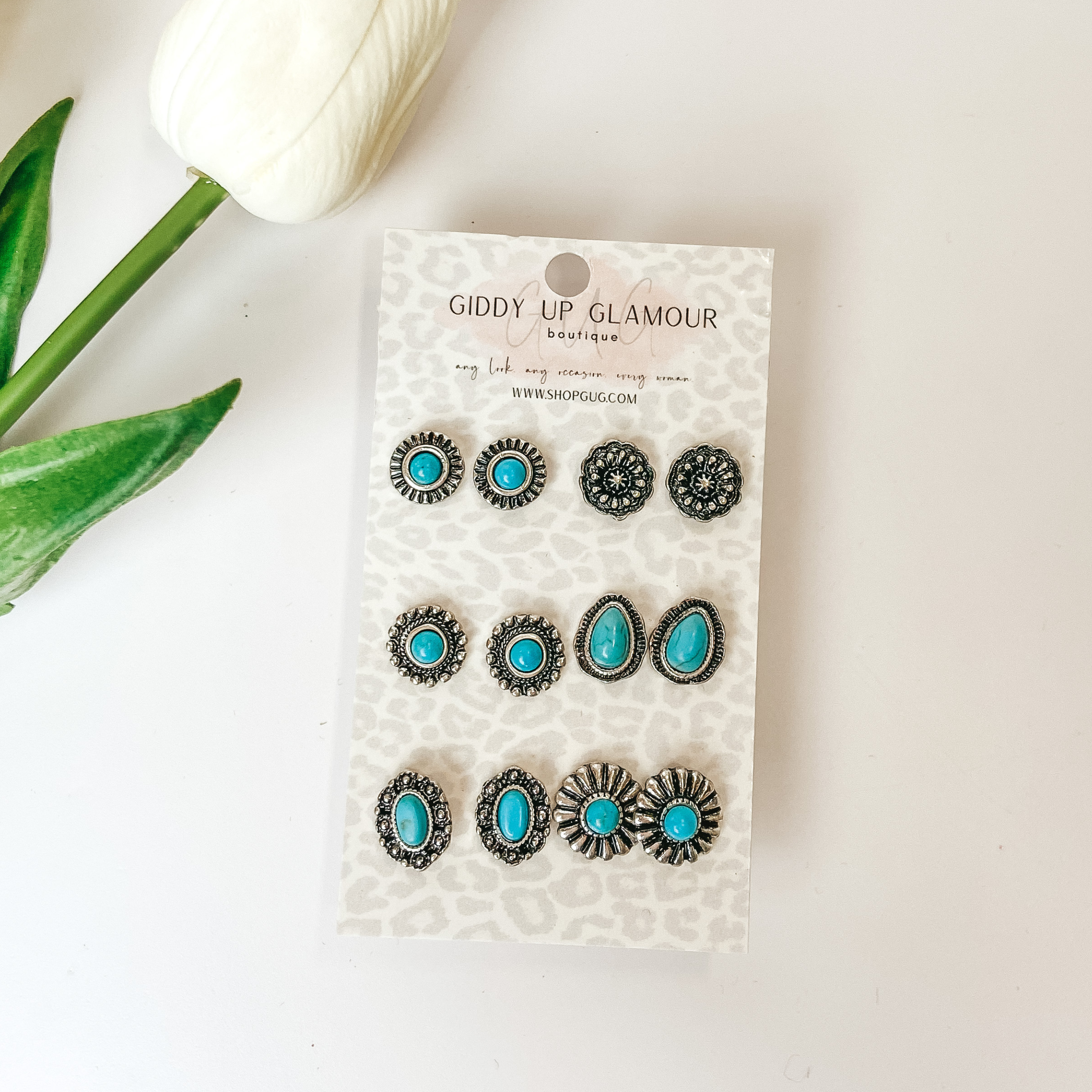 Set of six stud earrings. Sliver and turquoise small circular designs with a white background and white flower in the corner.