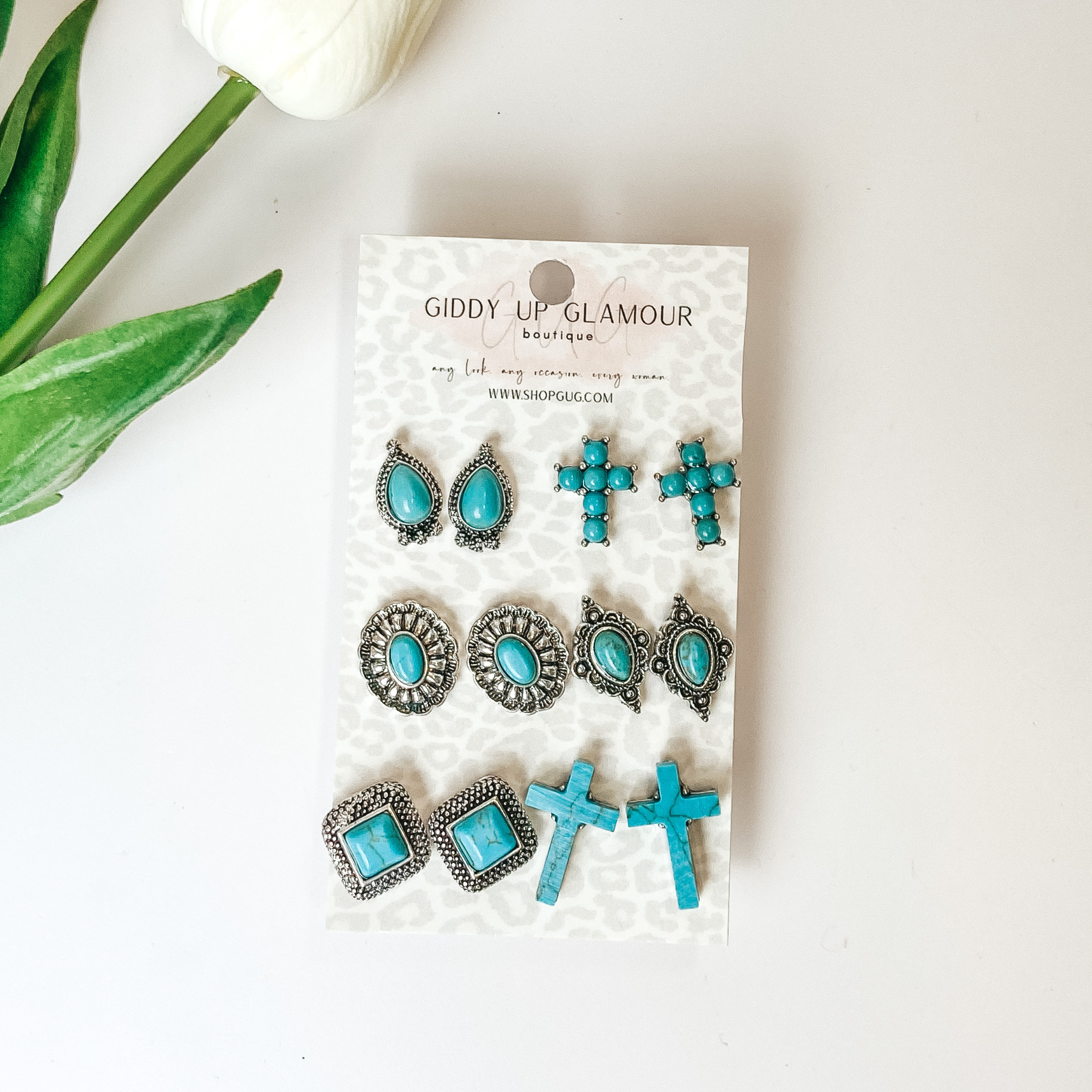 Six turquoise and silver designed stud earrings. Pictured on a white background with a white flower in the top left.