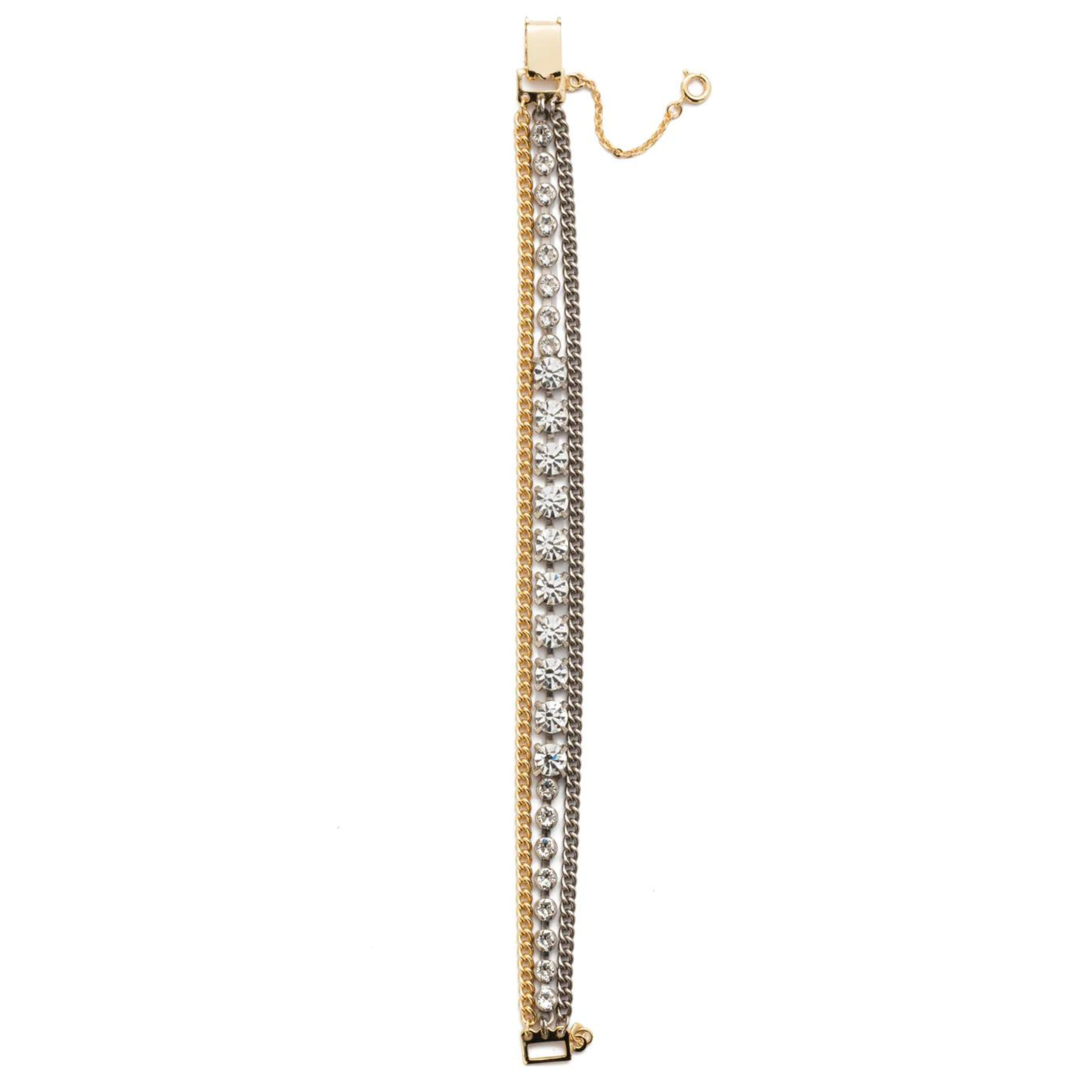Pictured is a bracelet with three different strands. One is a silver chain, a gold chain, and the center one has round, clear crystals. This bracelet includes gold hardware. This bracelet is pictured straight up and down on a white background. 