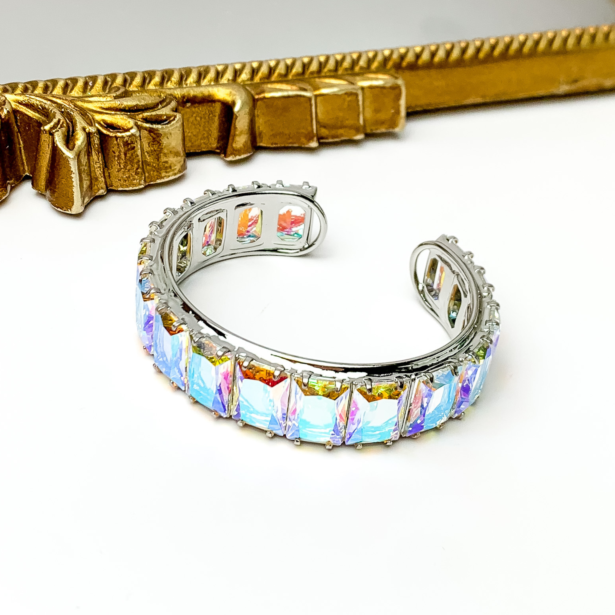 Silver bangle with a ab, rectangle crystal inlay. This bracelet is pictured on a white background with a gold mirror at the top of the picture.  