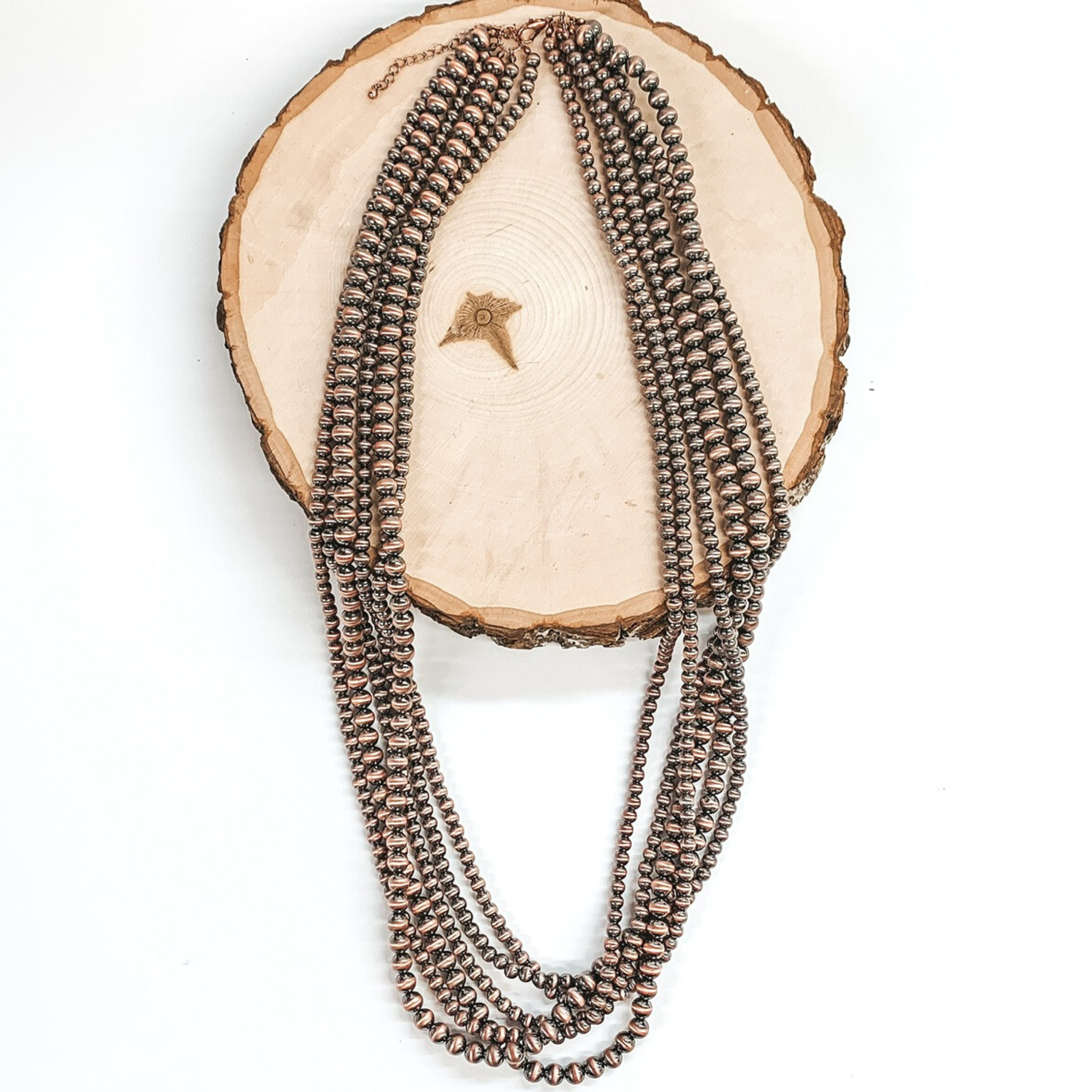 Multi stranded copper beaded, adjustable necklace. This necklace is half laying on a piece of wood on a white background.