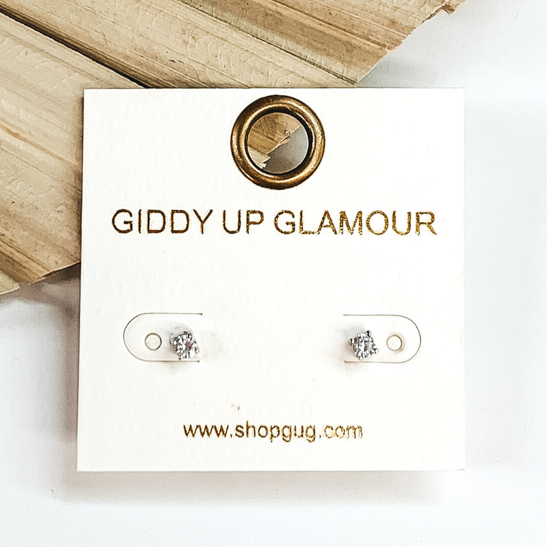 Clear crystal stud earrings. These earrings are pictured laying on a green palm leaf on a white background.