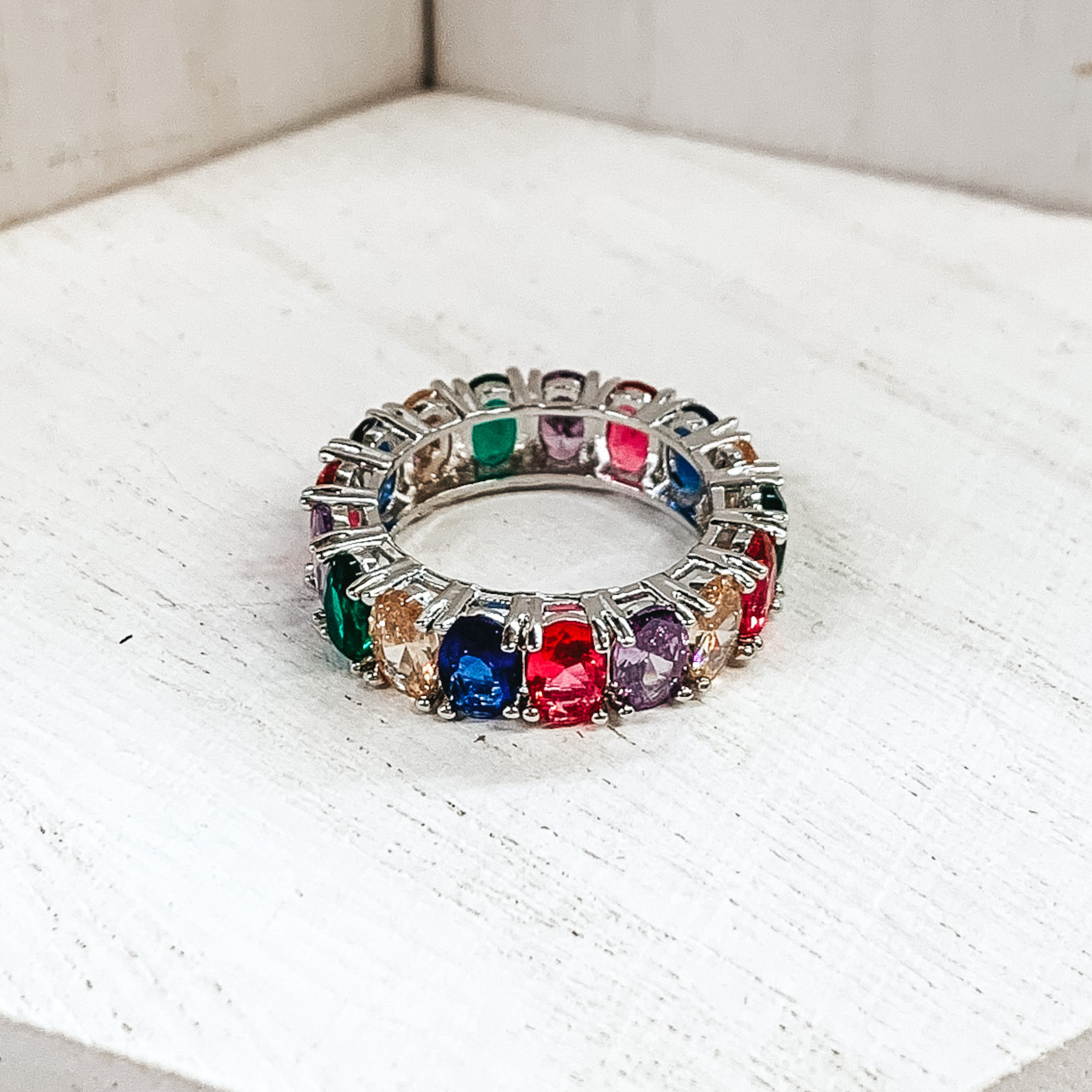 Silver ring with oval colored crystals around the entire ring. The crystals come in pink, blue, green, champagne, and purple shades. This ring is pictured on a white background.