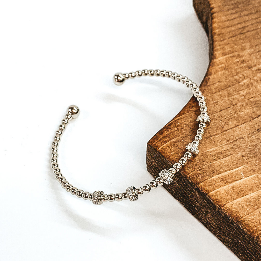 Gold beaded bangle bracelet with clear crystals spacers. This bangle is pictured leaning on a brown block on a white background.
