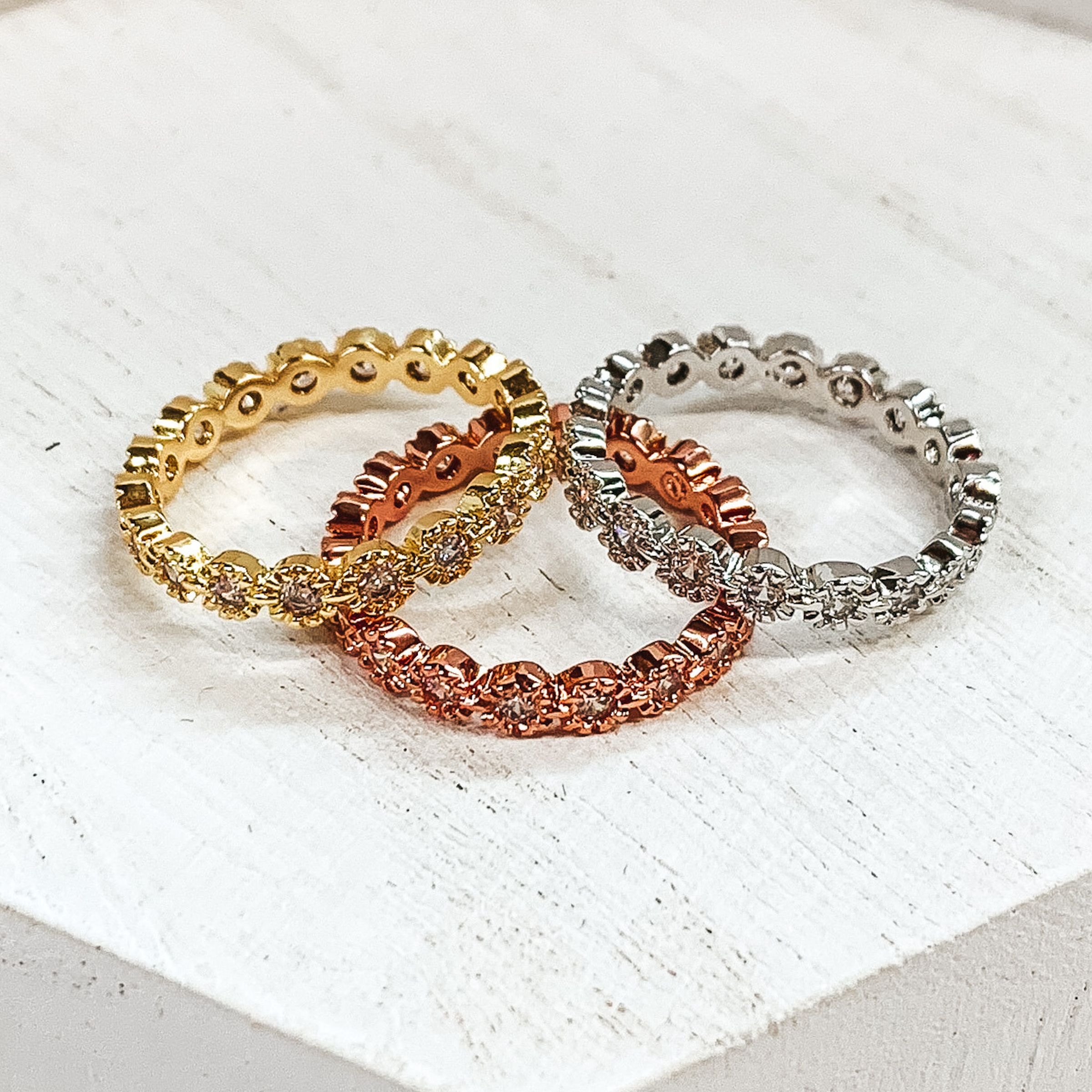 Set of three rings in silver, gold, and rose gold. Each is made of circles with center crystals in the color of the ring. These rings are pictured on a white background.