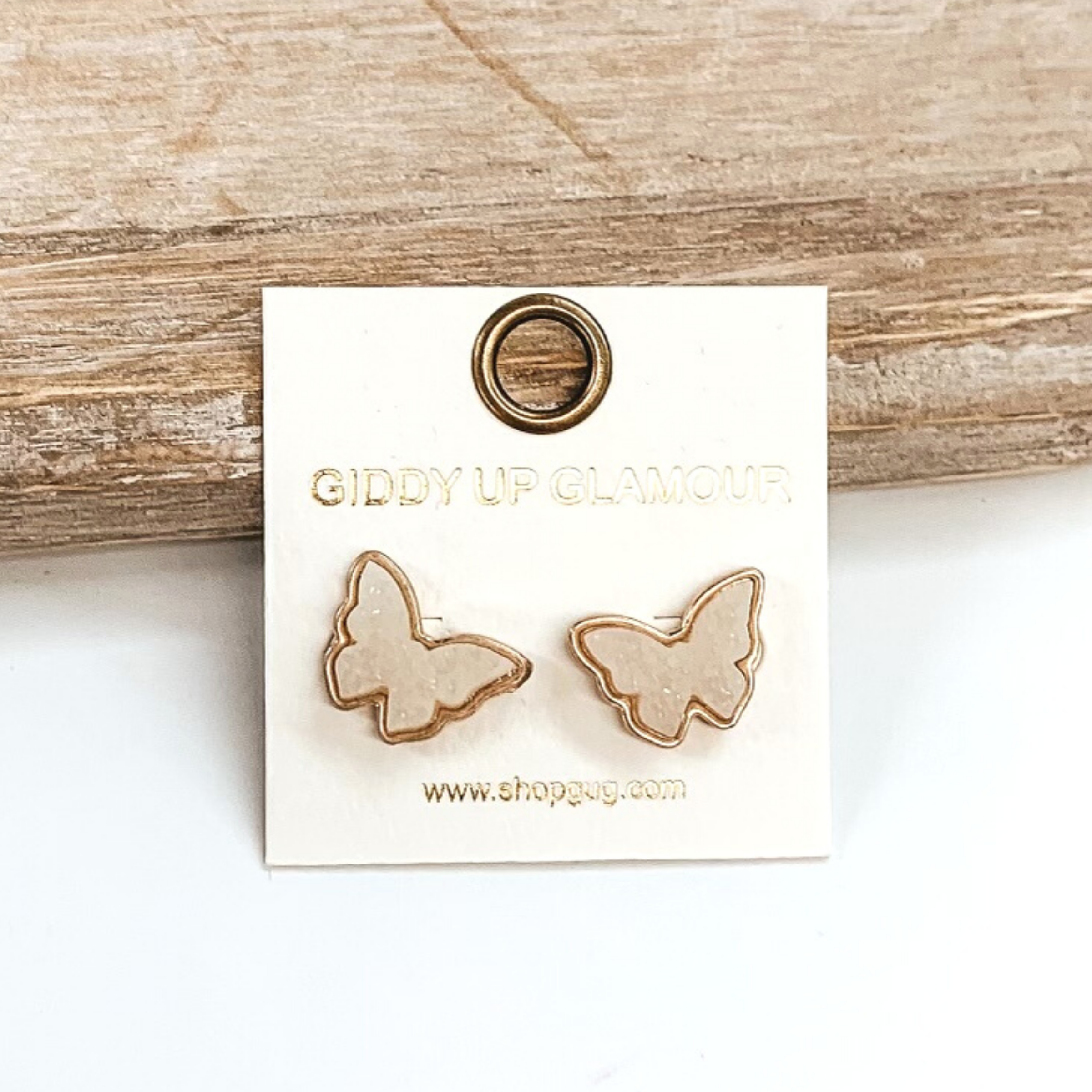 Gold post back earrings with druzy, white, butterfly shaped stone. These earrings are pictured on a white earrings holder on a white background, leaning against a tan block