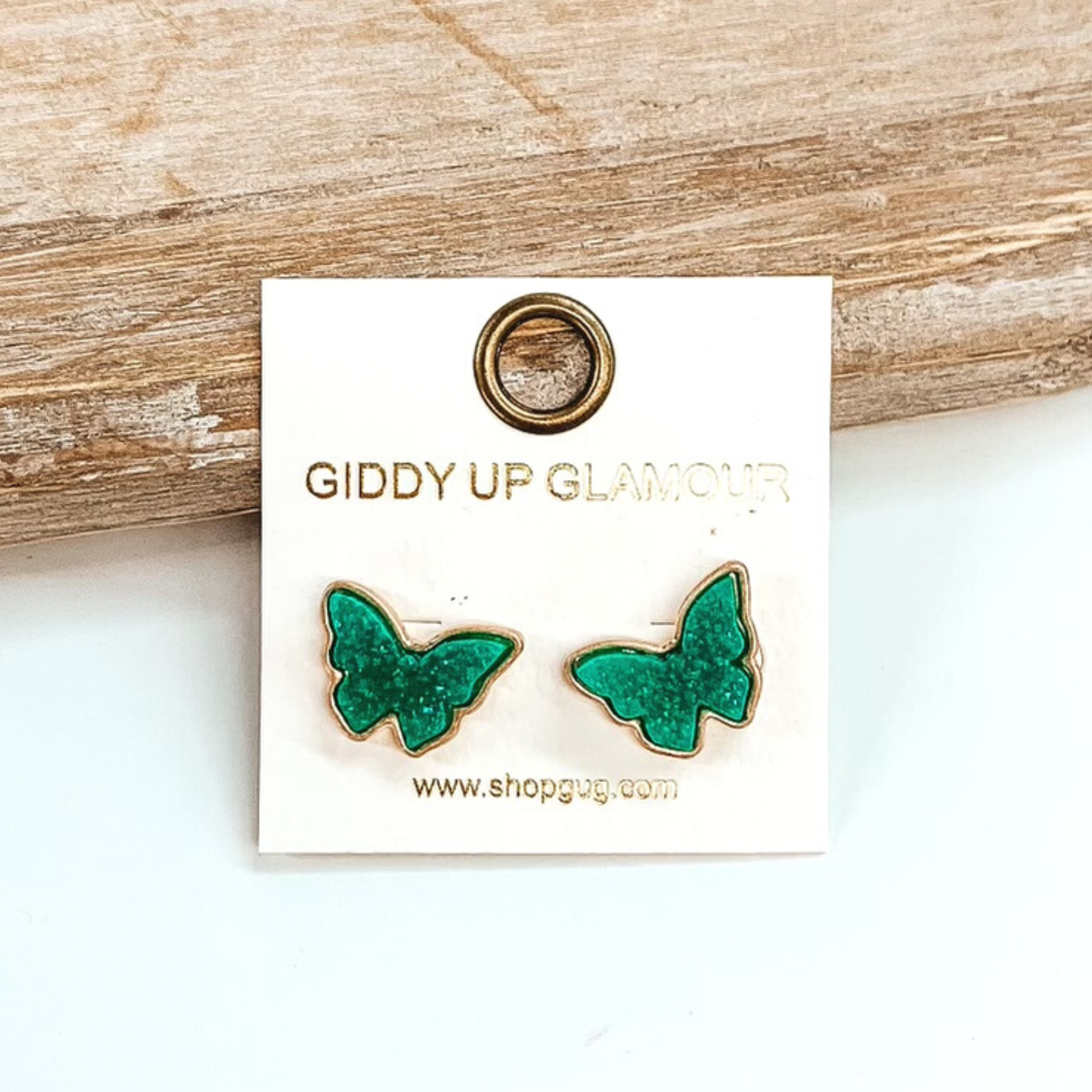 Gold post back earrings with druzy, turquoise, butterfly shaped stone. These earrings are pictured on a white earrings holder on a white background, leaning against a tan block.