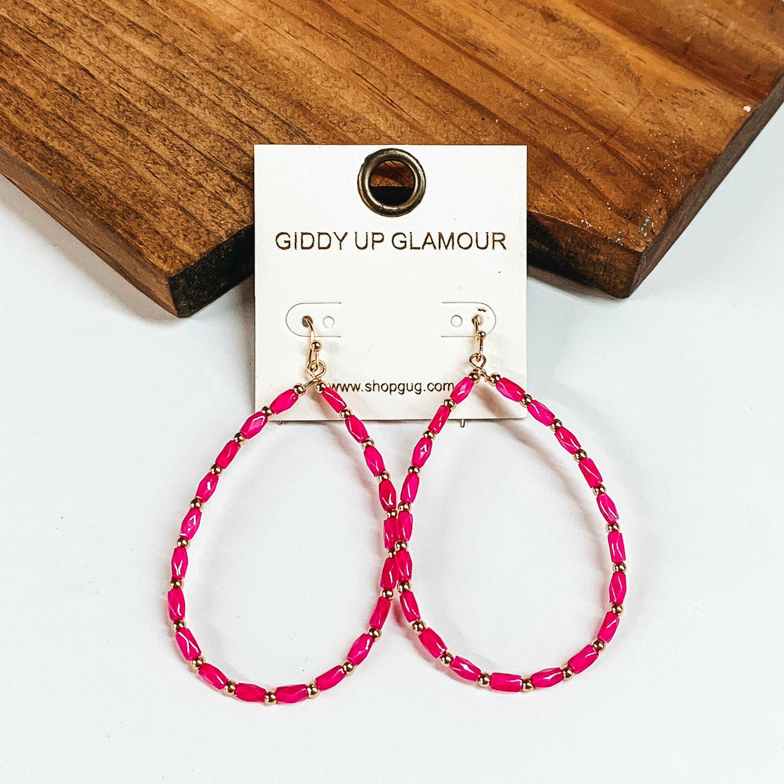 Hot pink beads spaced with gold round beads create a teardrop earrings that is perfect for everyone! The earrings are placed on white and wood board. 