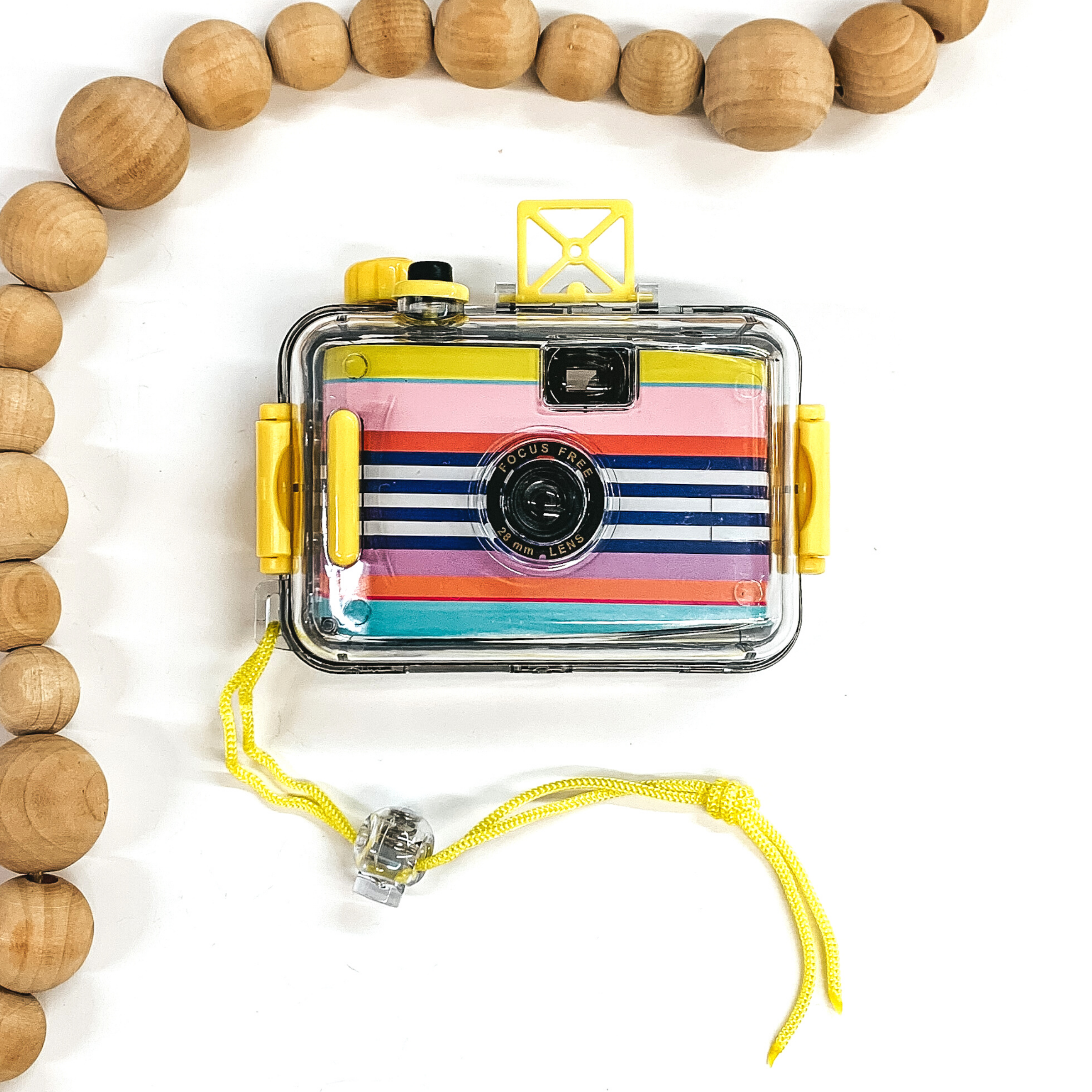 Multicolored striped camera in a clear case with yellow accents. This camera is pictured on a white background with tan beads around the top left corner. 