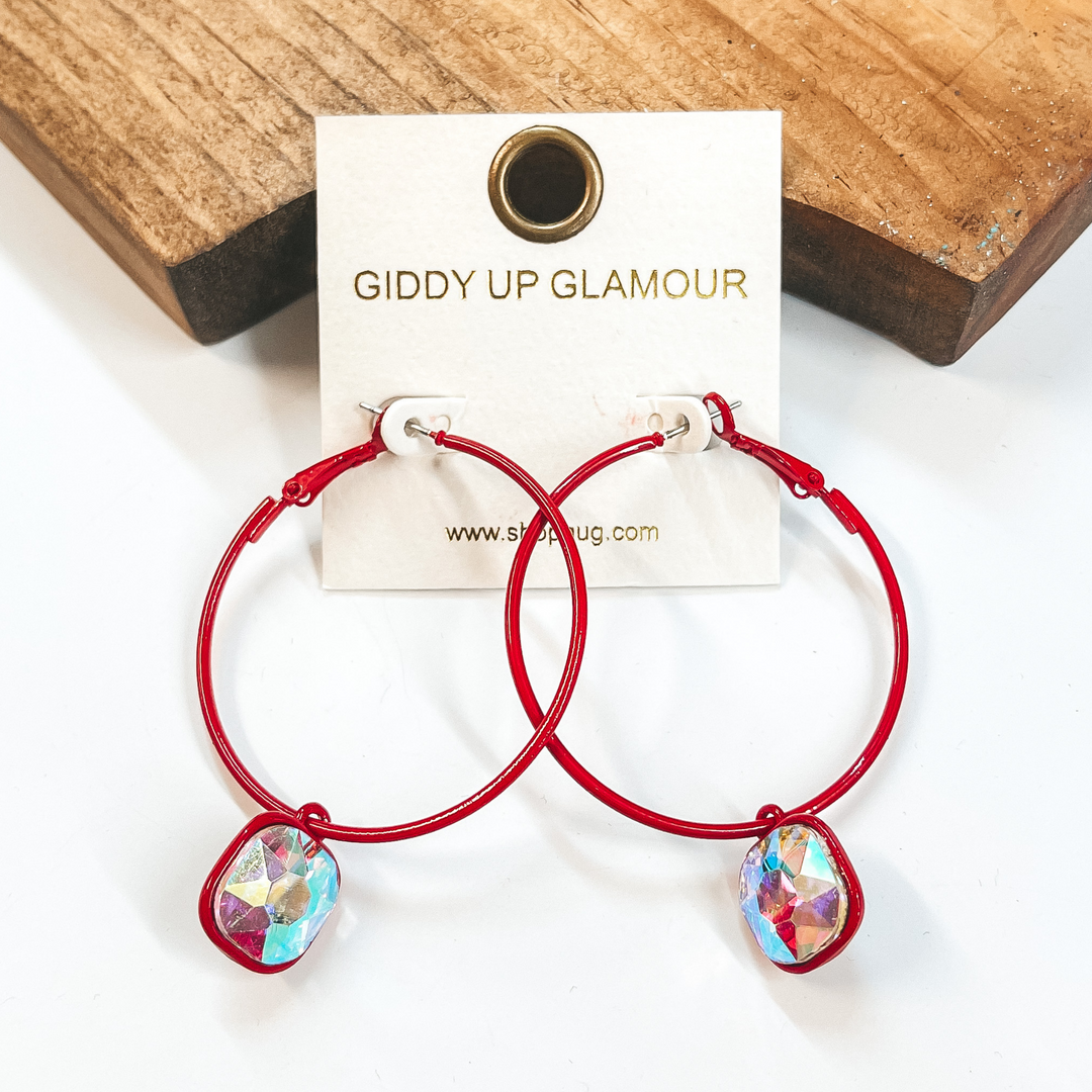 Circle hoop earrings in red with a cushion cut AB crystal drop. Taken on a white background and leaned up against  a brown block.