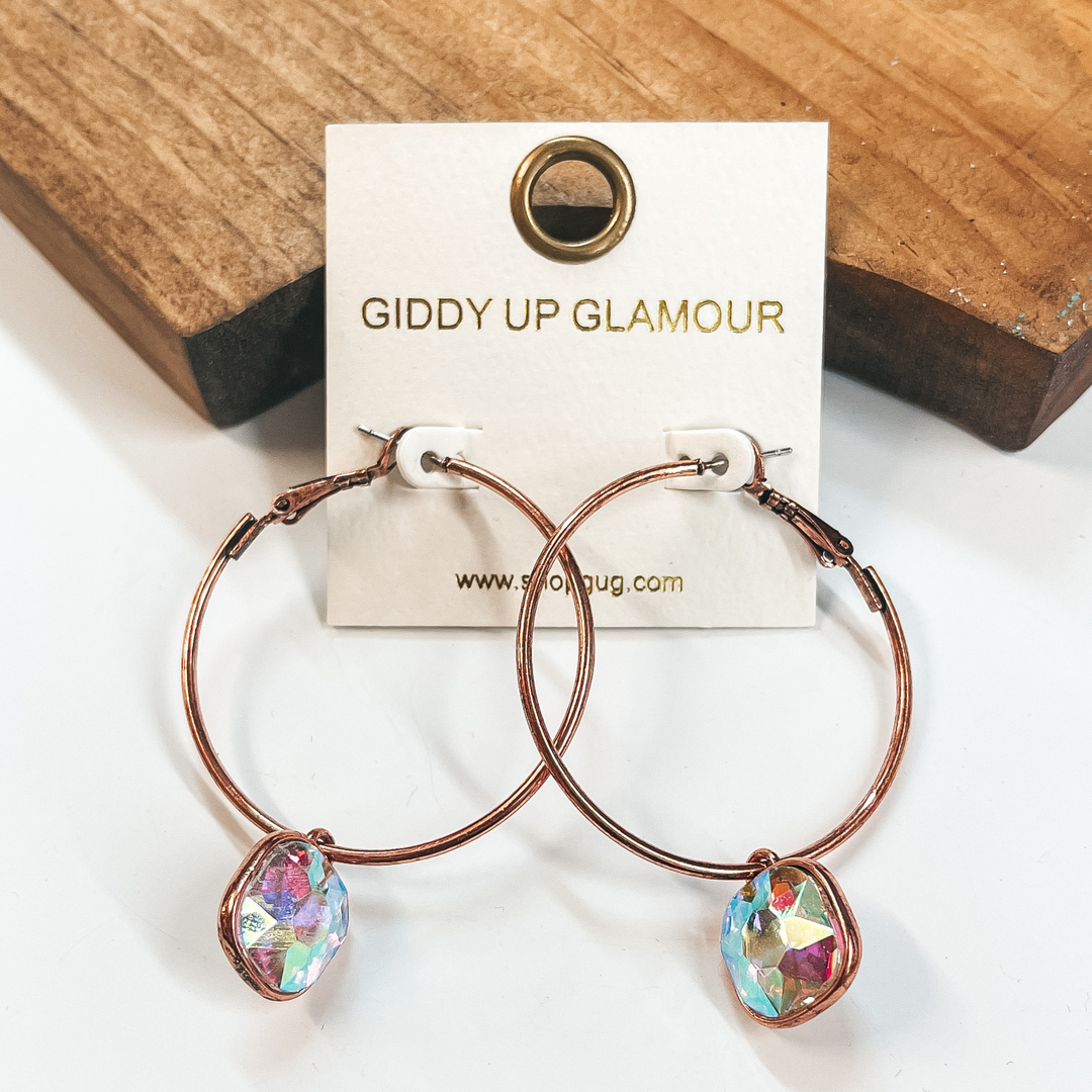 Circle hoop earrings in copper with a cushion cut AB crystal drop. Taken on a white background and leaned up against  a brown block.