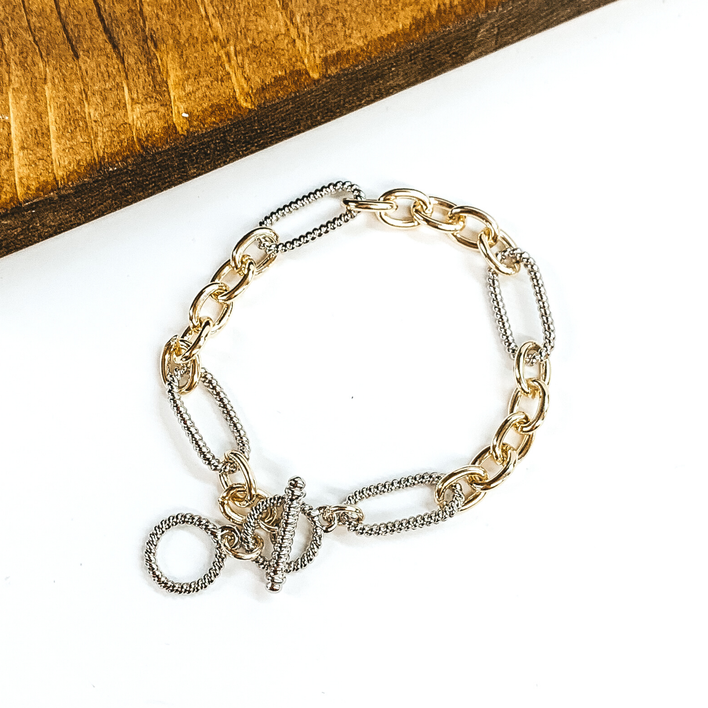Thin, twisted, silver chains linked with small, thin gold chains. This bracelet has a toggle clasp. This bracelet is pictured on a white background. 