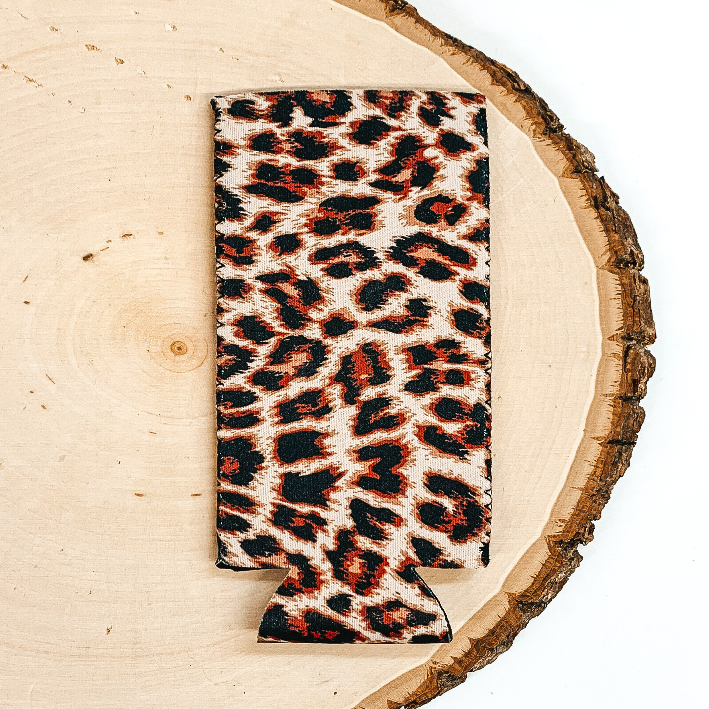 Leopard print slim can koozie pictured laying on a piece of wood on a white background.