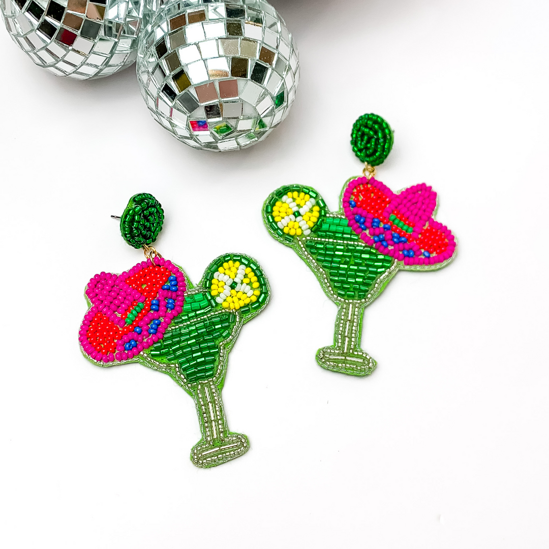 Margarita sombrero seed beaded drop earrings in green. The sombrero has orange, dark blue, and pink sequins. Taken in a white background with disco balls in the left corner.