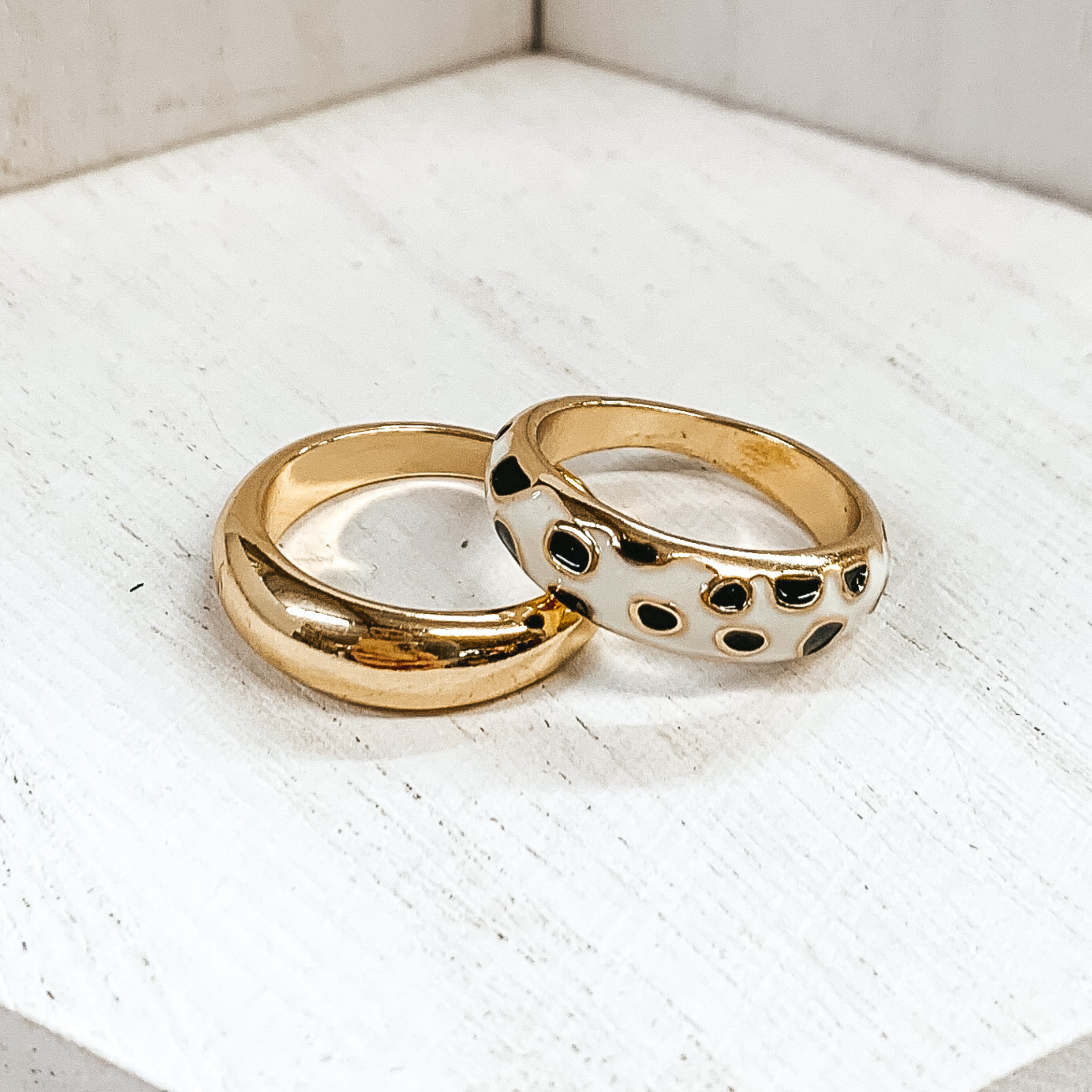 Set of two thick, gold rings. One ring is plain, while the secong ring has a white colored part with black cheetah print. These rings are pictured on a white background. 