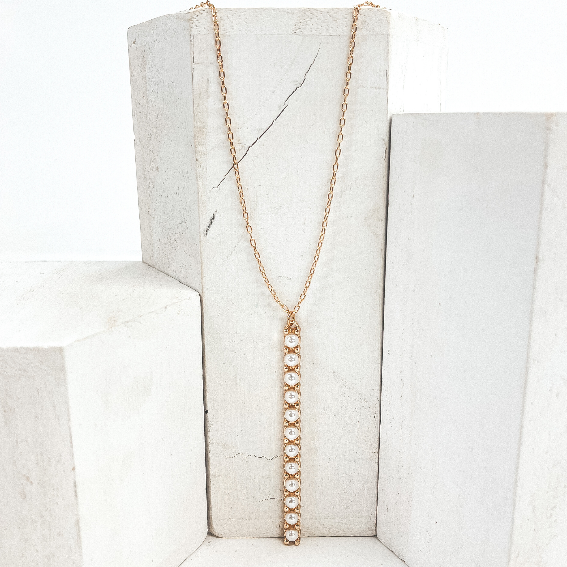This is a 30 inch adjustable gold necklace with  a gold 2.75 inch bar pendant with pearls. This  necklace is pictured laying on a white block  on a white background with one white block on  each side.