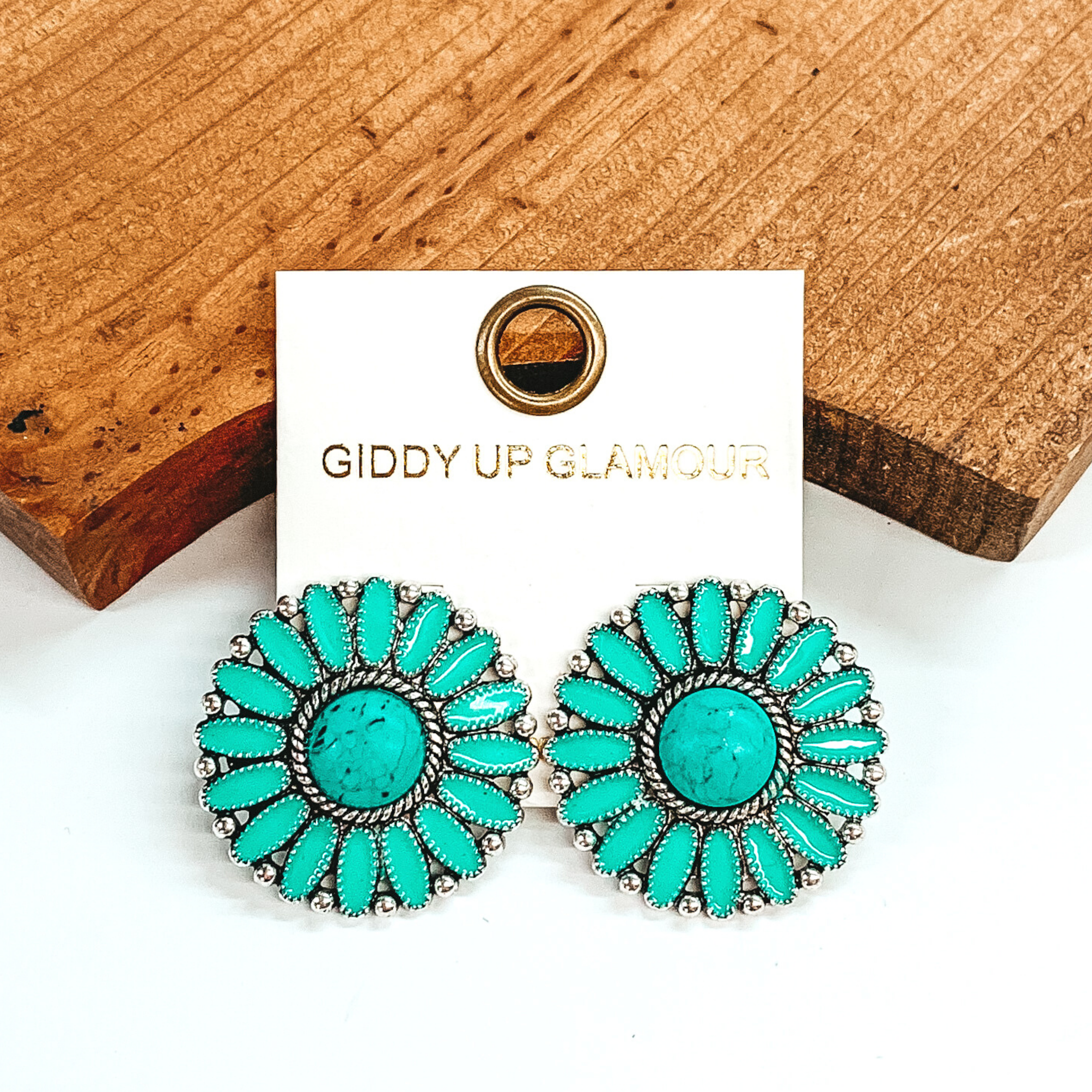 Turquoise concho earrings with a center turquoise stone and silver outline. These earrings are pictured on a white earrings holder laying against a dark brown block on a white background. 