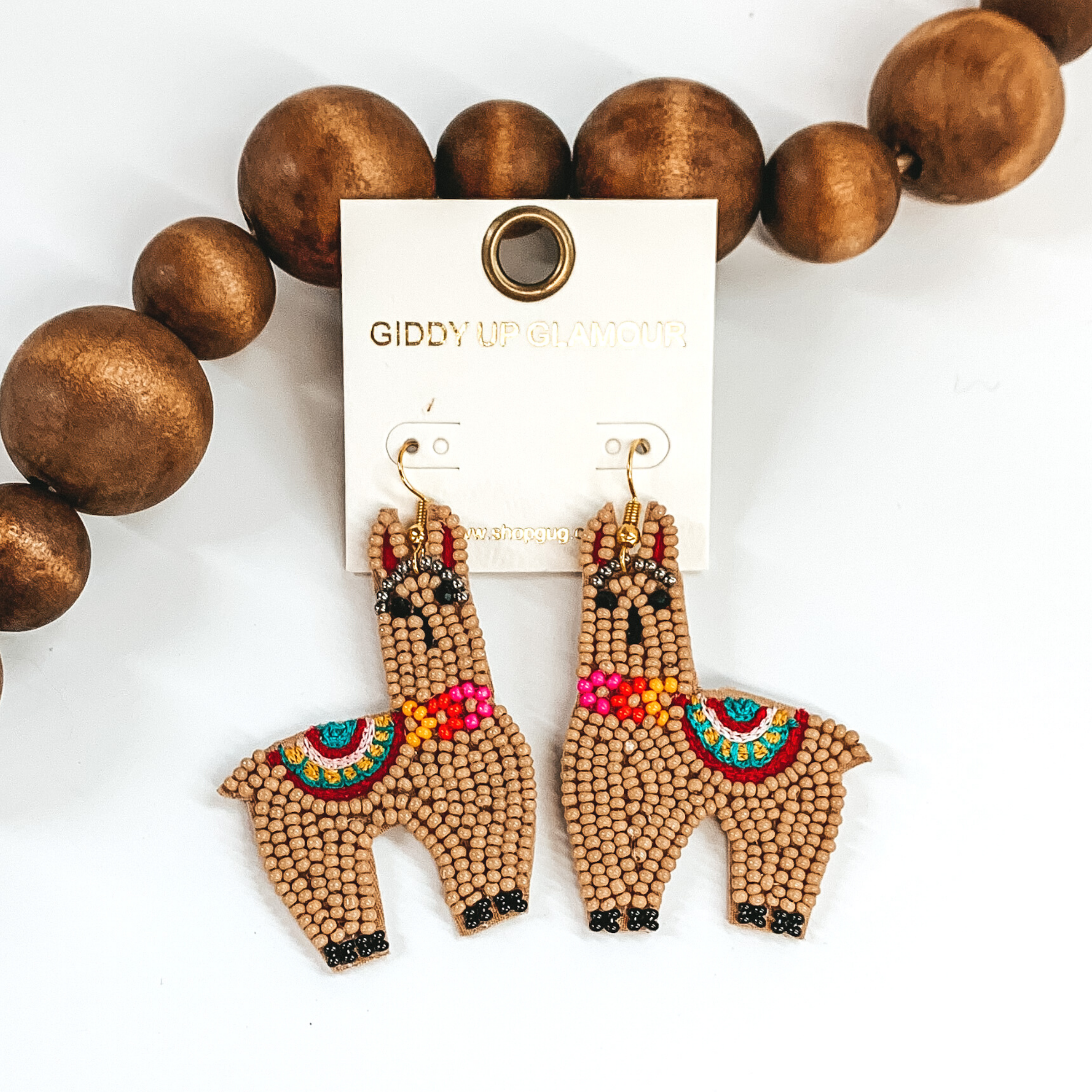 Llama shaped beaded dangle earrings in tan. These earrings also includes some colorful stitching details. These earrings are pictured on a white background with dark brown beads towards the top of the picture.