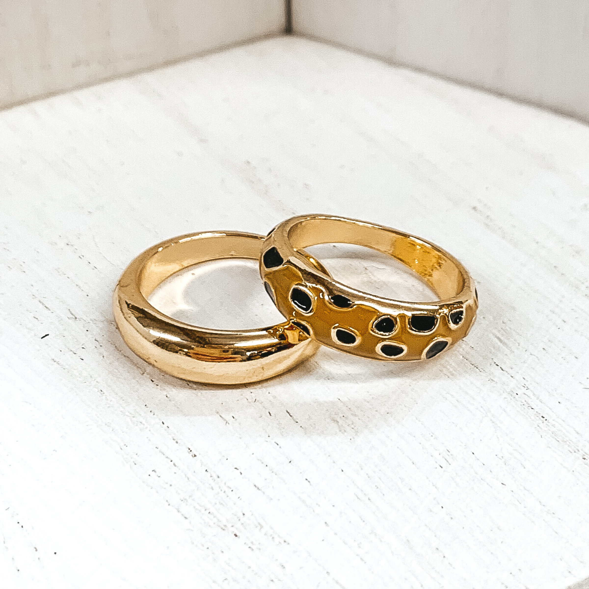 Set of two thick, gold rings. One ring is plain, while the secong ring has a tan colored part with black cheetah print. These rings are pictured on a white background. 