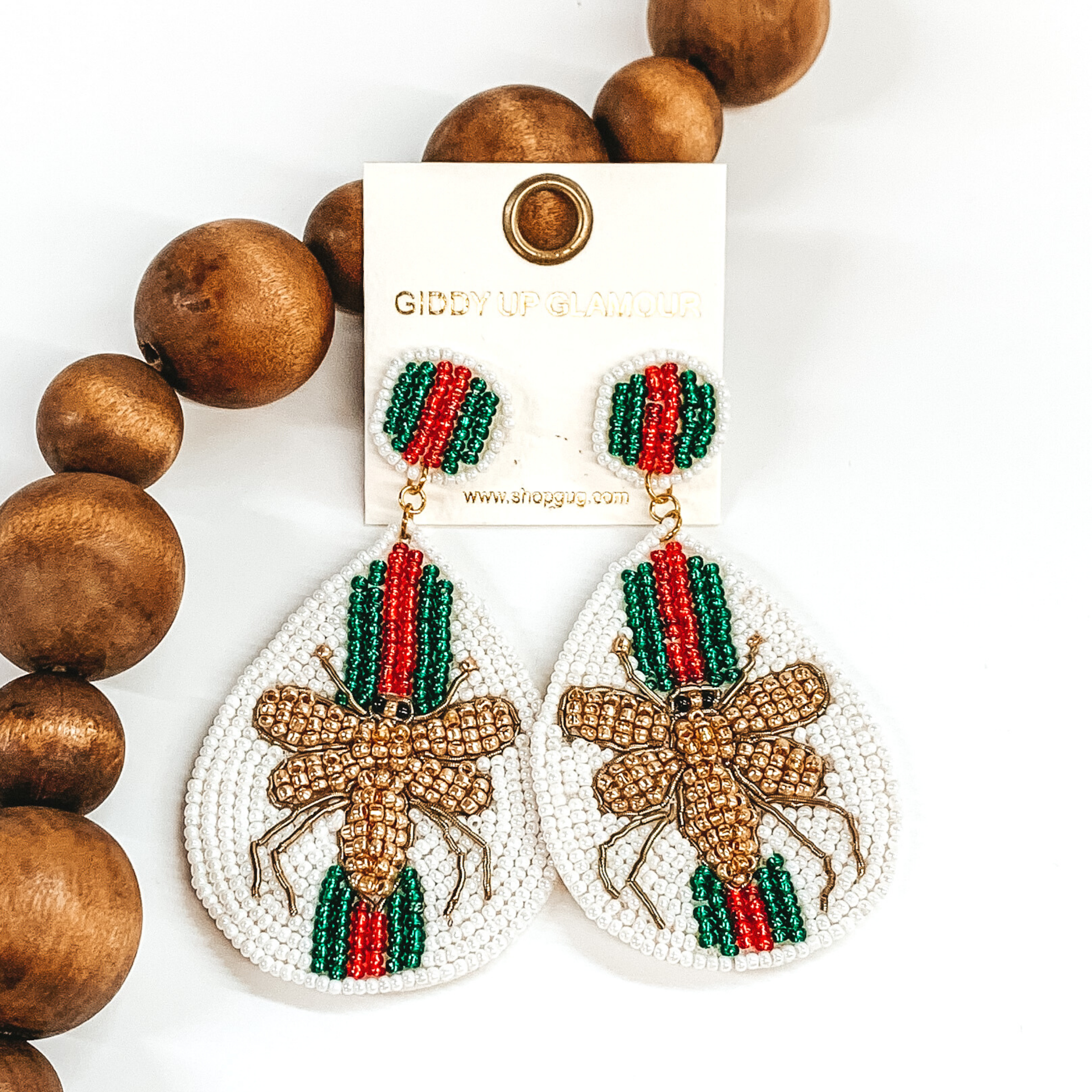 Circle beaded studs with a beaded teardrop dangle. The majority of the beads were ivory with green and red stripes. The center of the teardrop was a gold beaded bee. These earrings are pictured on a white background with dark brown beads.