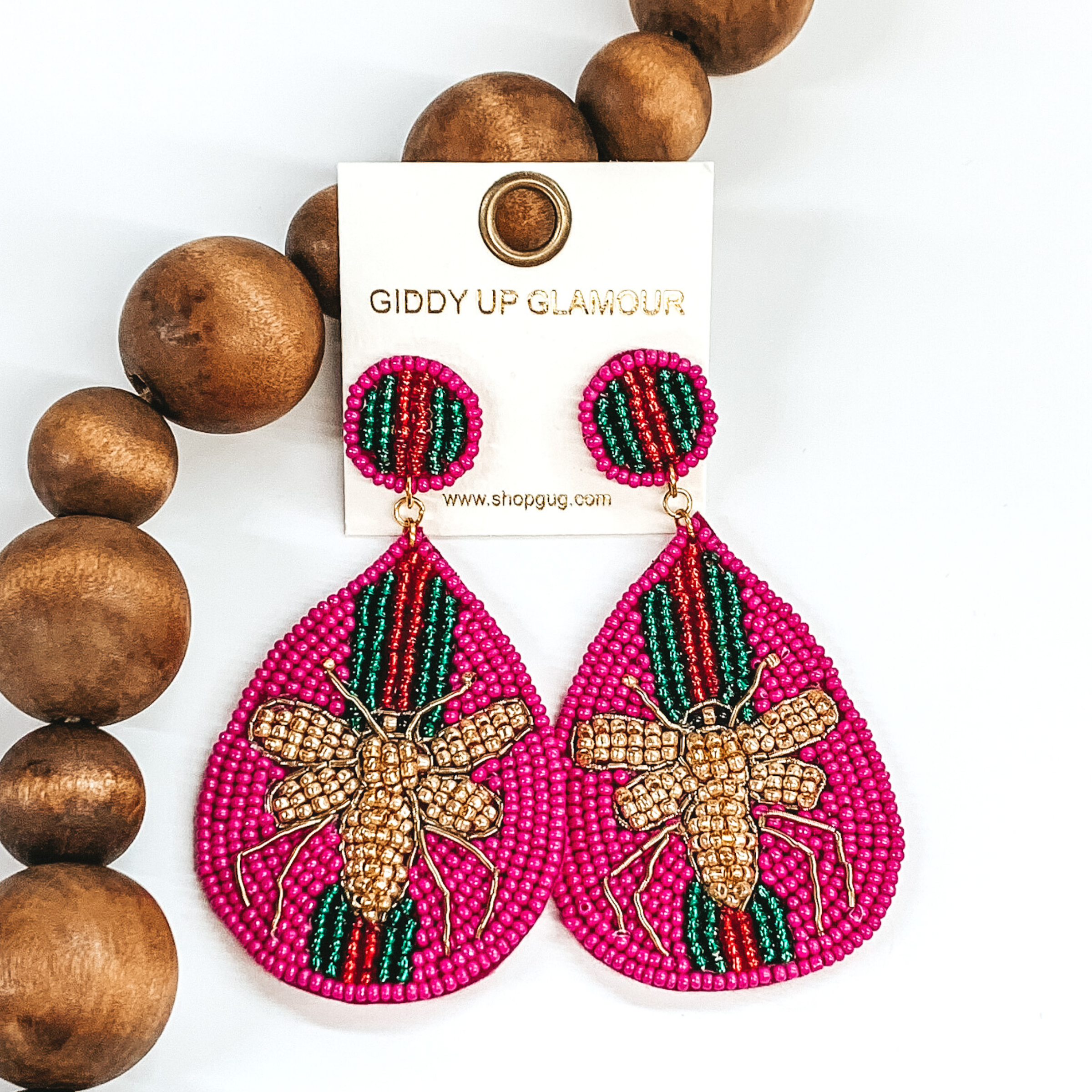 Circle beaded studs with a beaded teardrop dangle. The majority of the beads were fuchsia with green and red stripes. The center of the teardrop was a gold beaded bee. These earrings are pictured on a white background with dark brown beads.