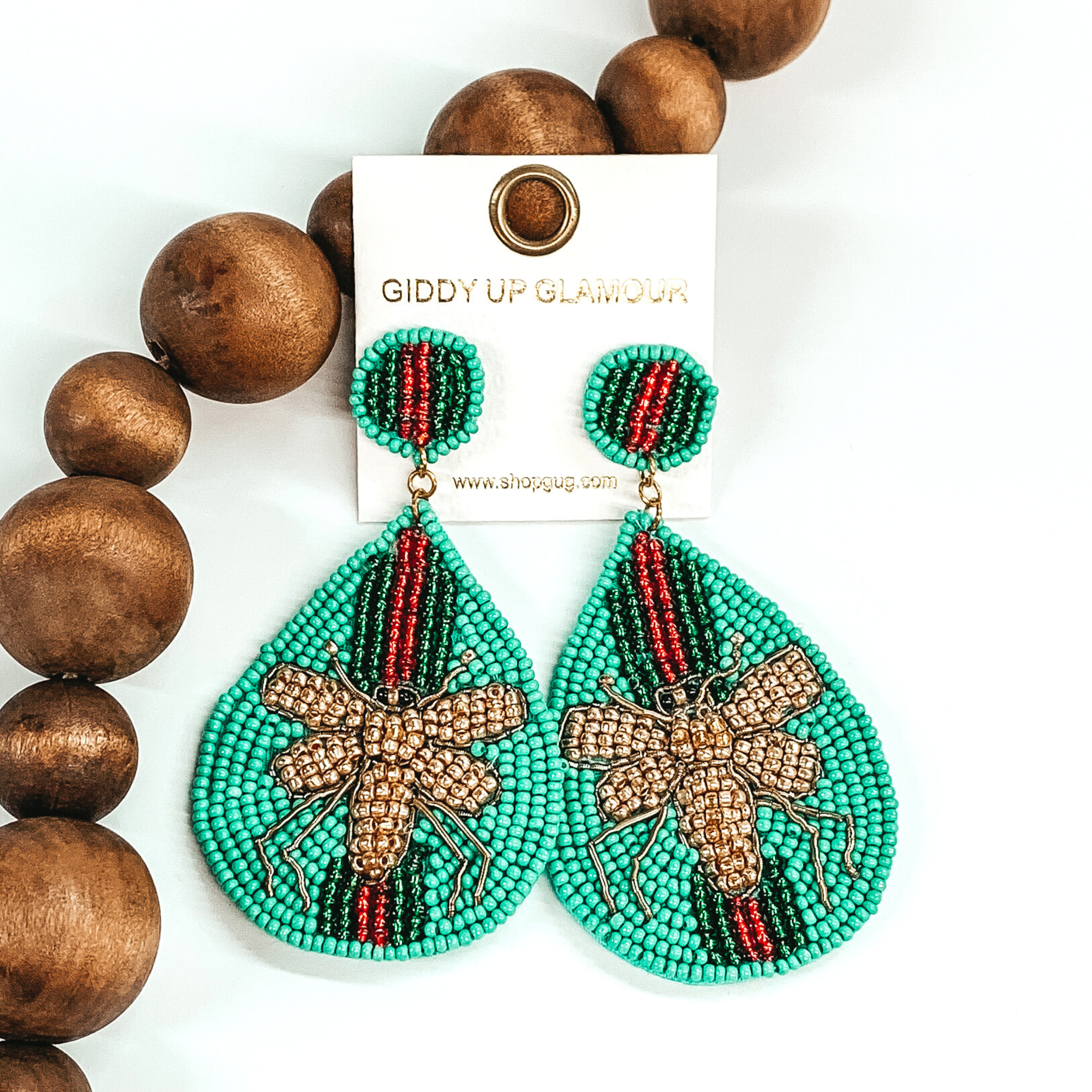 Circle beaded studs with a beaded teardrop dangle. The majority of the beads were turquoise with green and red stripes. The center of the teardrop was a gold beaded bee. These earrings are pictured on a white background with dark brown beads.