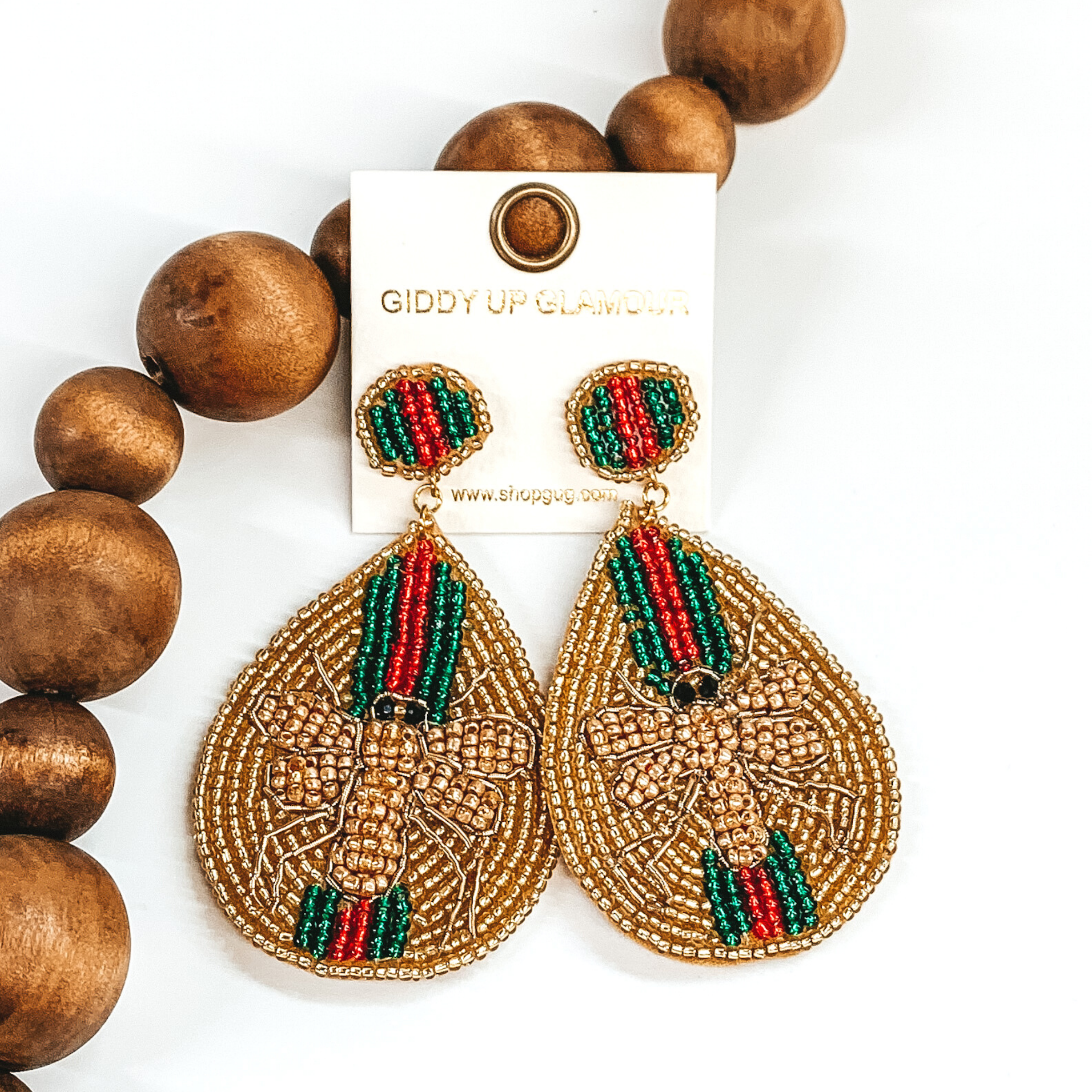 Circle beaded studs with a beaded teardrop dangle. The majority of the beads were gold with green and red stripes. The center of the teardrop was a gold beaded bee. These earrings are pictured on a white background with dark brown beads.