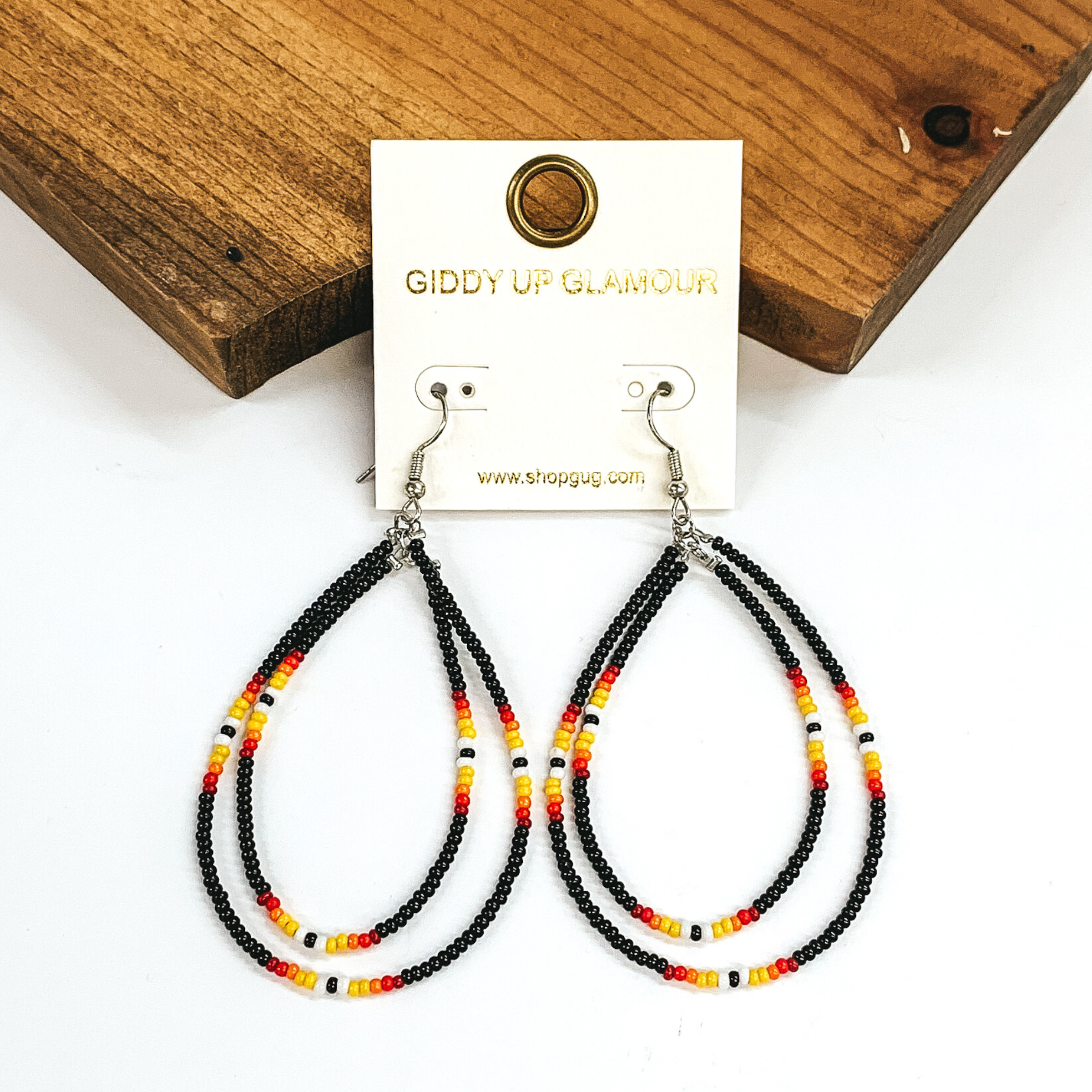 Double layered, hanging beaded teardrop earrings. The majority of the beads are black with three segements including maroon, red, yellow, white, and black beads. hese earrigns are pictured on a white background in front of a dark piece of wood. 