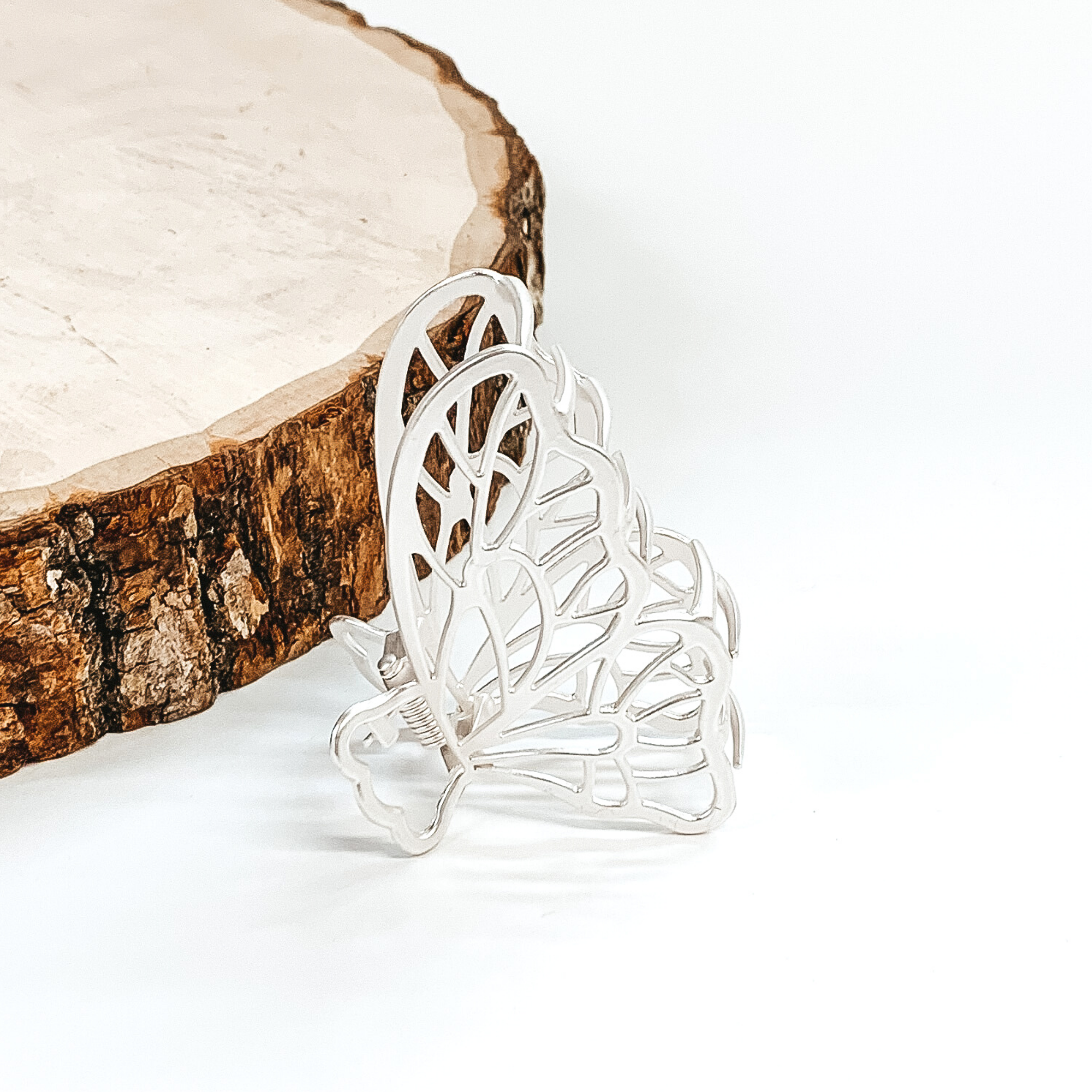Matte silver, butterfly shaped hair clip. This clip is pictured in front of a piece of wood on a white background. 