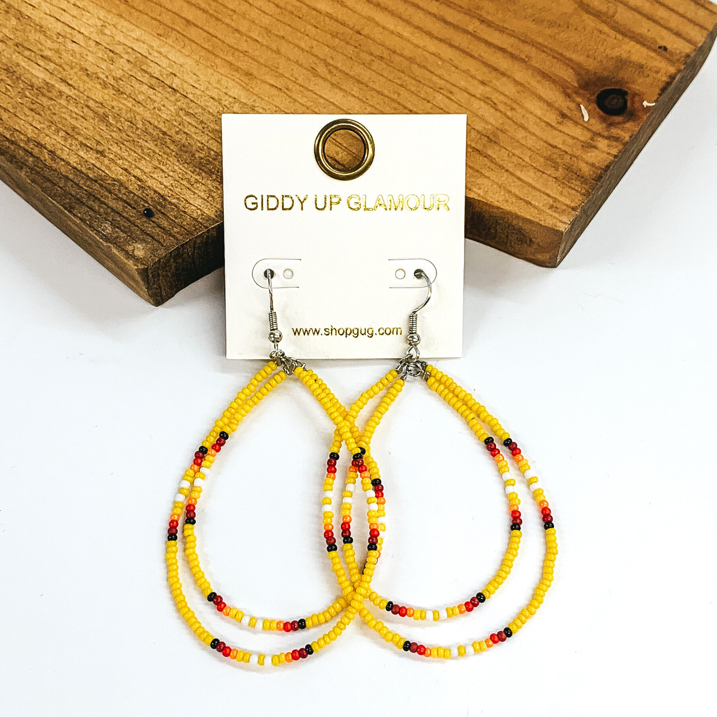 Double layered, hanging beaded teardrop earrings. The majority of the beads are yellow with three segements including maroon, red, yellow, white, and black beads. hese earrings are pictured on a white background in front of a dark piece of wood. 