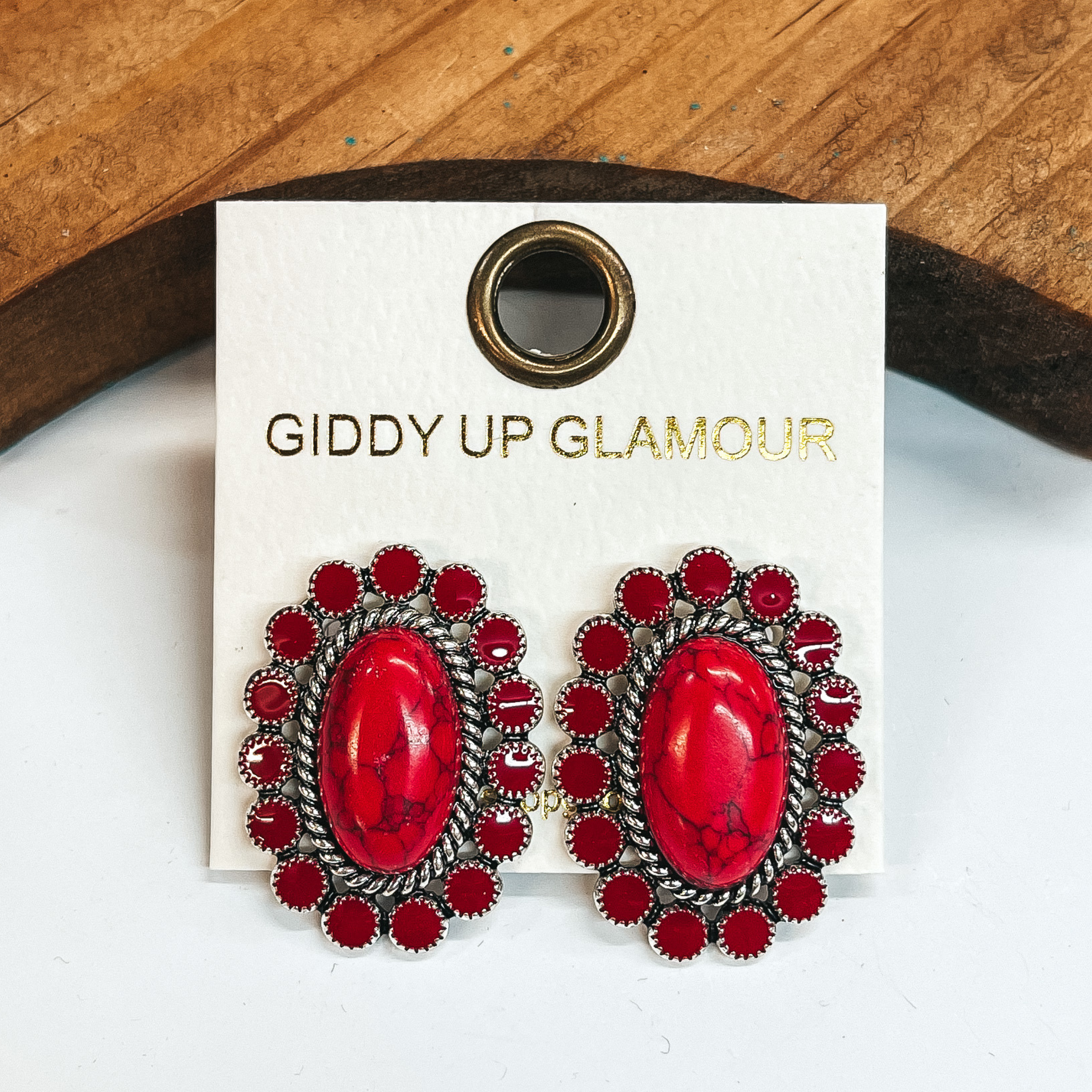 Dark red concho earrings outlined by silver  detailing and dark red circles around.  Taken on a white background and leaned up against a brown block.