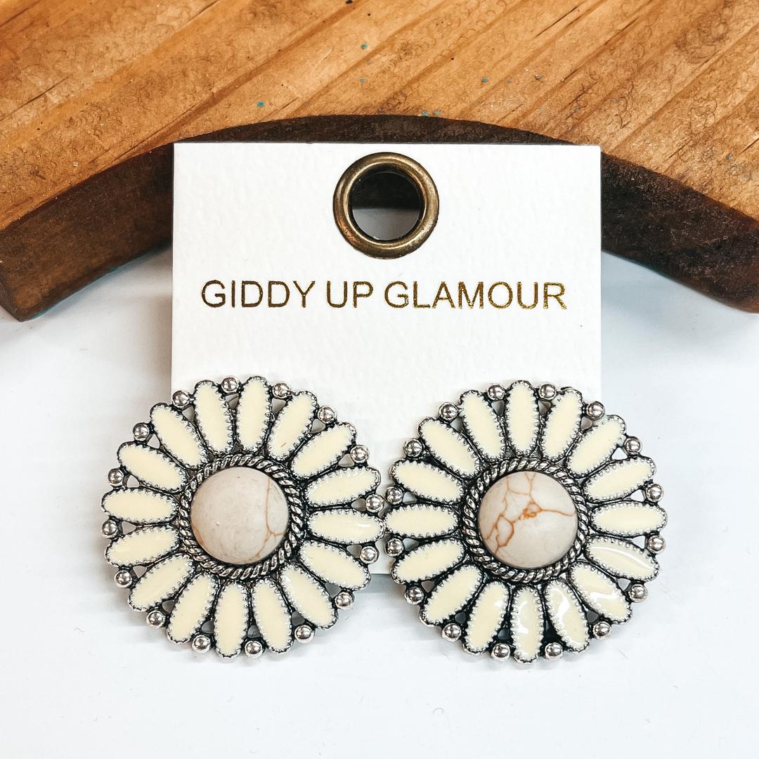 Ivory concho earrings with a center ivory stone and  silver outline. These earrings are pictured leaning  up against a brown block with a white background.