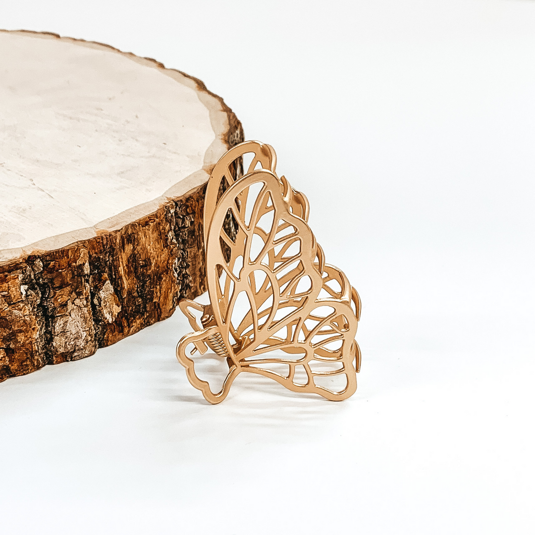 Matte gold, butterfly shaped hair clip. This clip is pictured in front of a piece of wood on a white background.