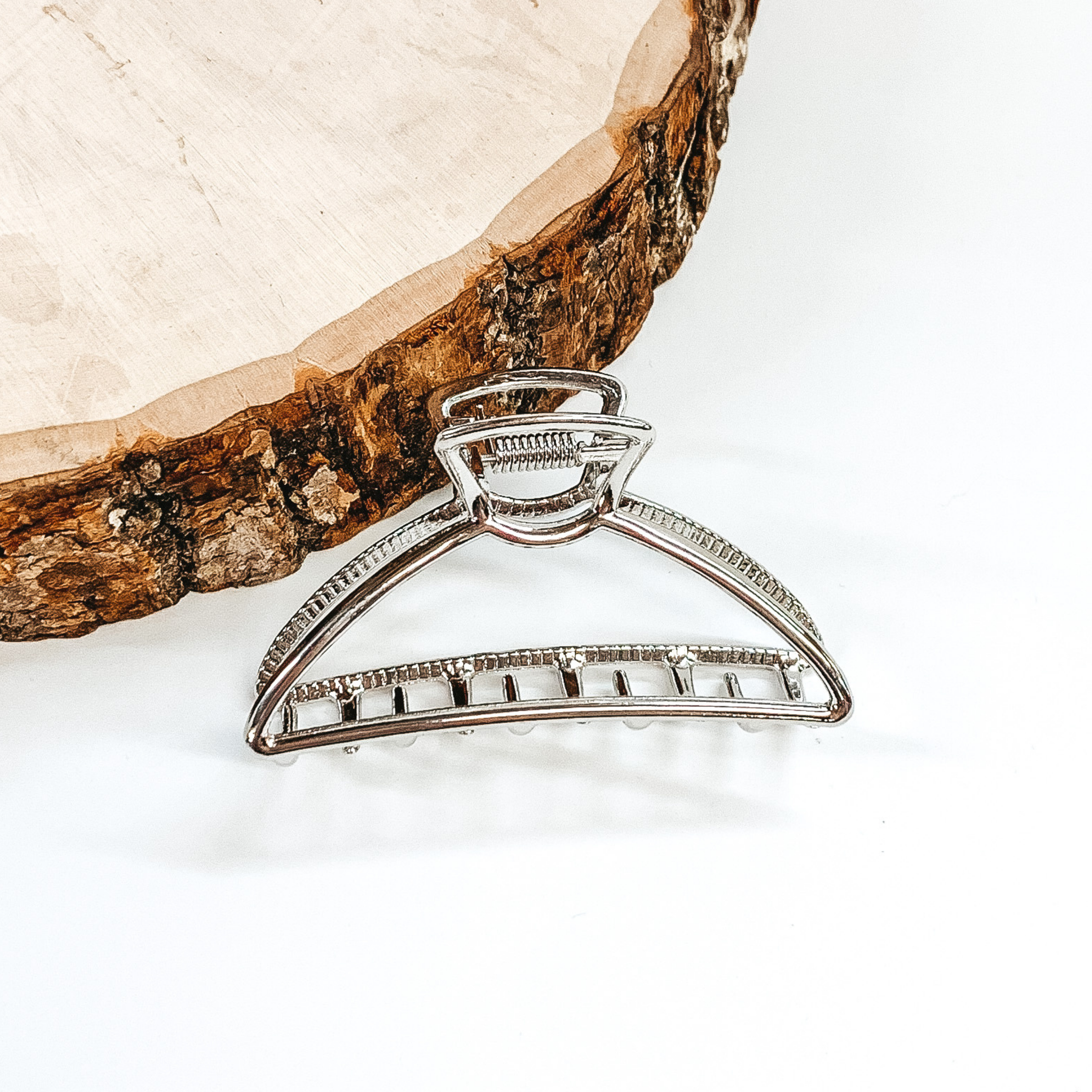 Shiny silver, rounded, open triangle clip. This clip is pictured in front of a piece of wood on a white background. 