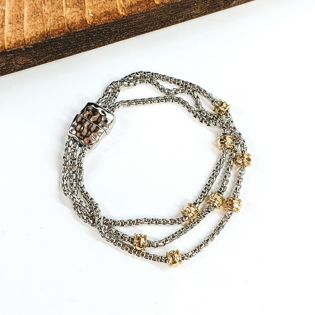 Silver, three stranded bracelet with gold spacers. This bracelet has a magnetic clasp. This bracelet is pictured on a white background.