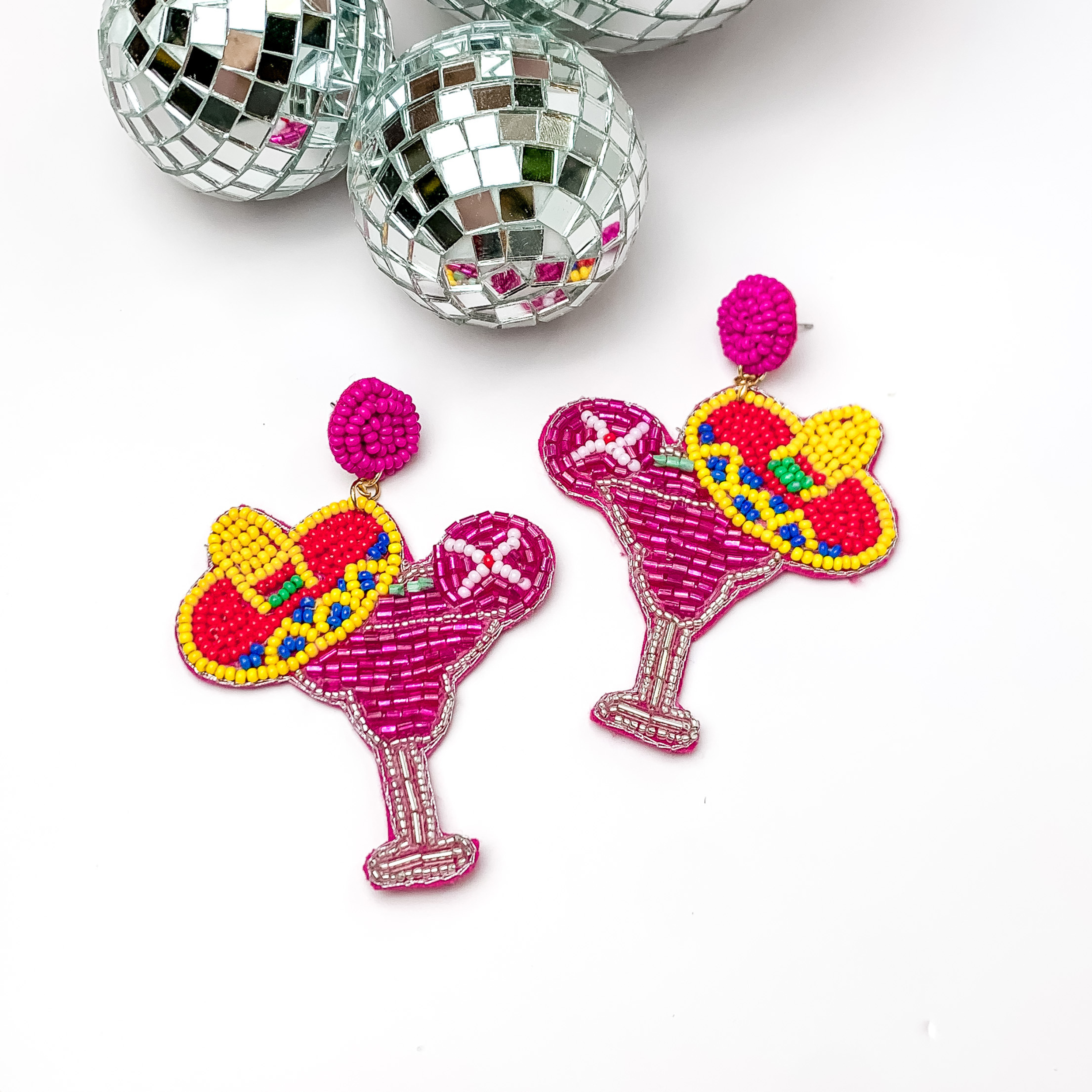 Margarita sombrero seed beaded drop earrings in pink. The sombrero has yellow, dark blue, and red sequins. Taken in a white background with disco balls in the left corner.