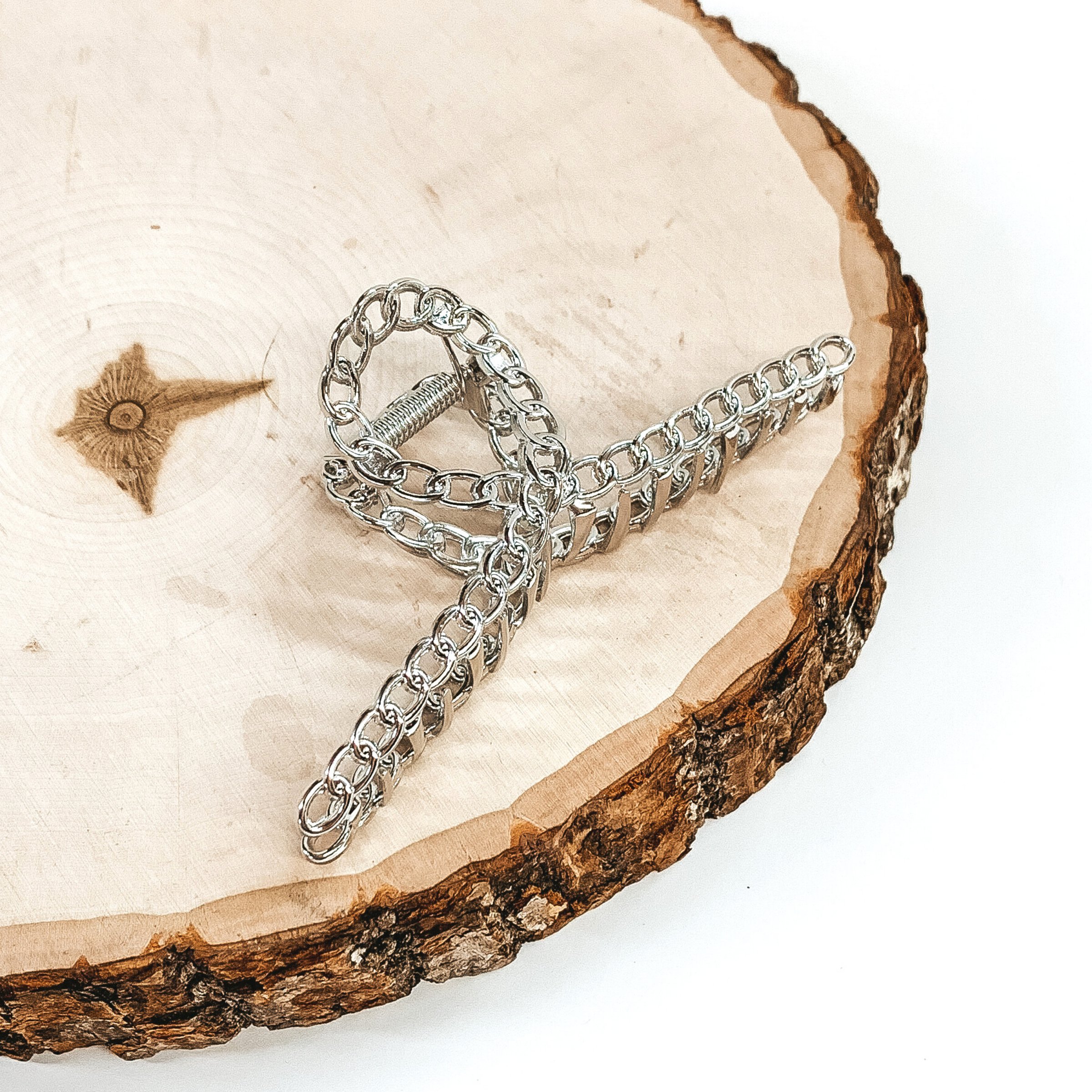 Shiny silver, chain linked clip. This clip is pictured laying on a piece of wood on a white background. 