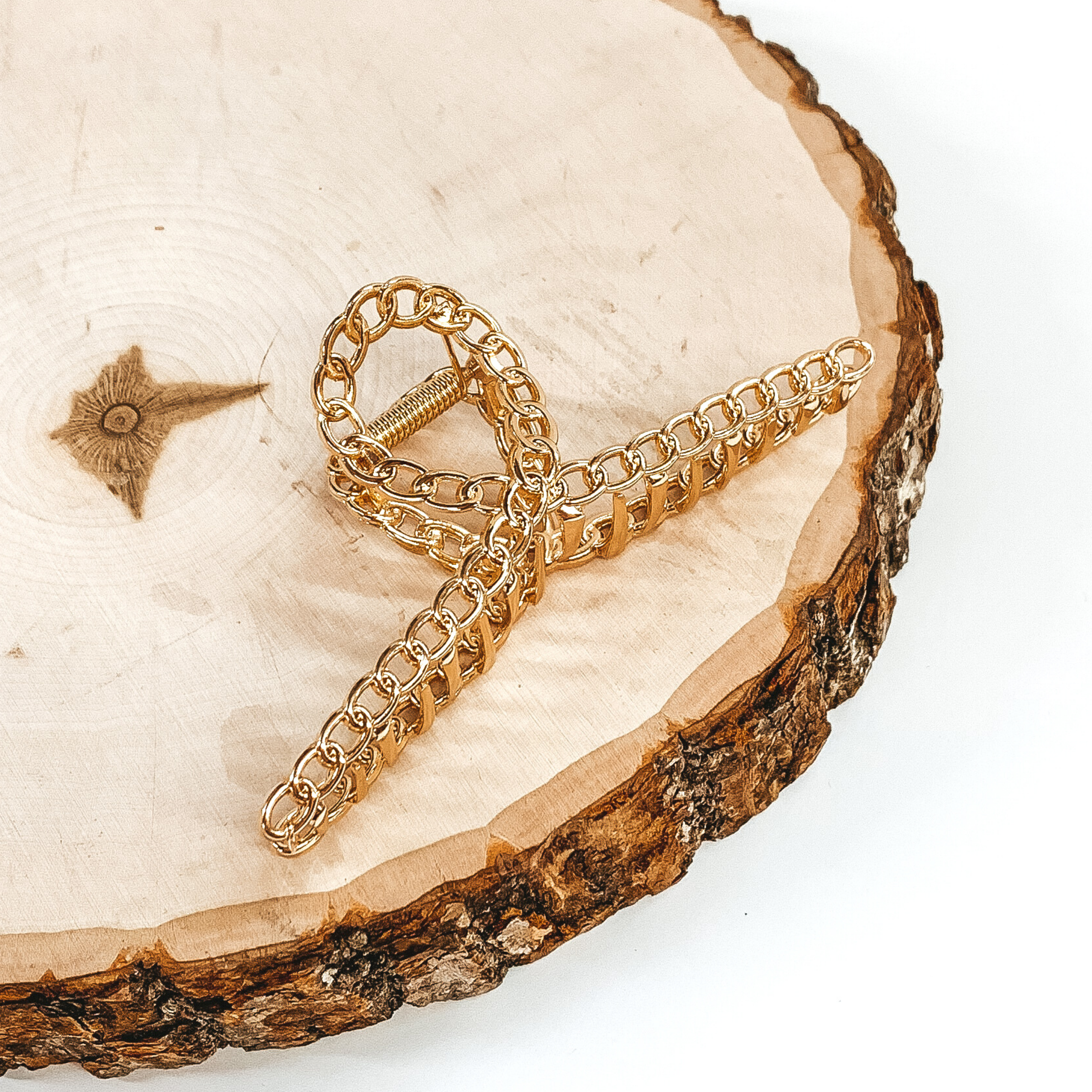 Shiny gold, chain linked clip. This clip is pictured laying on a piece of wood on a white background.