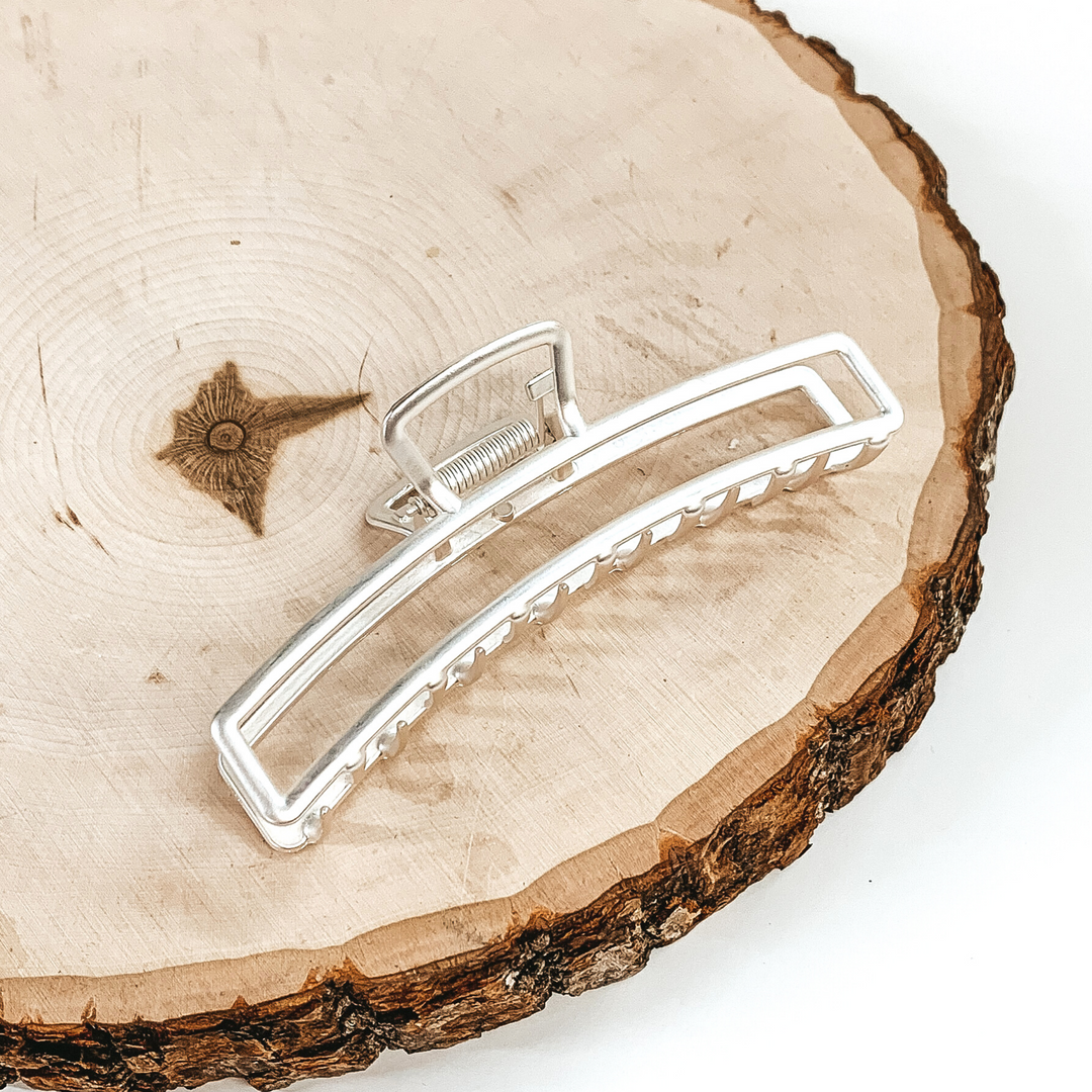 Matte silver, long, thin, open rectangle slip. This clip is pictured laying on a piece of wood on a white background. 