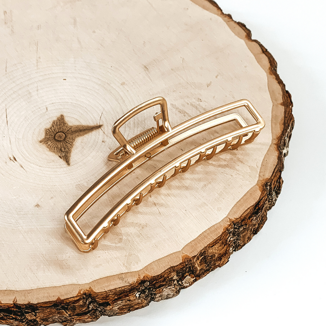 Matte gold, long, thin, open rectangle slip. This clip is pictured laying on a piece of wood on a white background.