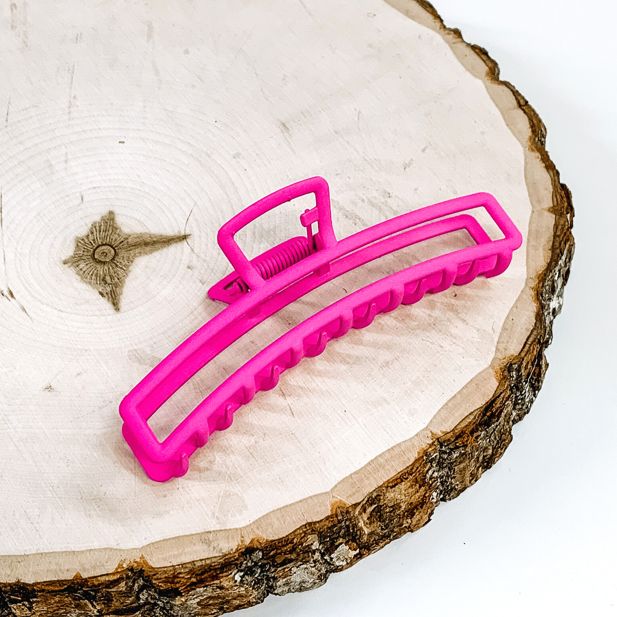 Matte pink, long, thin, open rectangle slip. This clip is pictured laying on a piece of wood on a white background.
