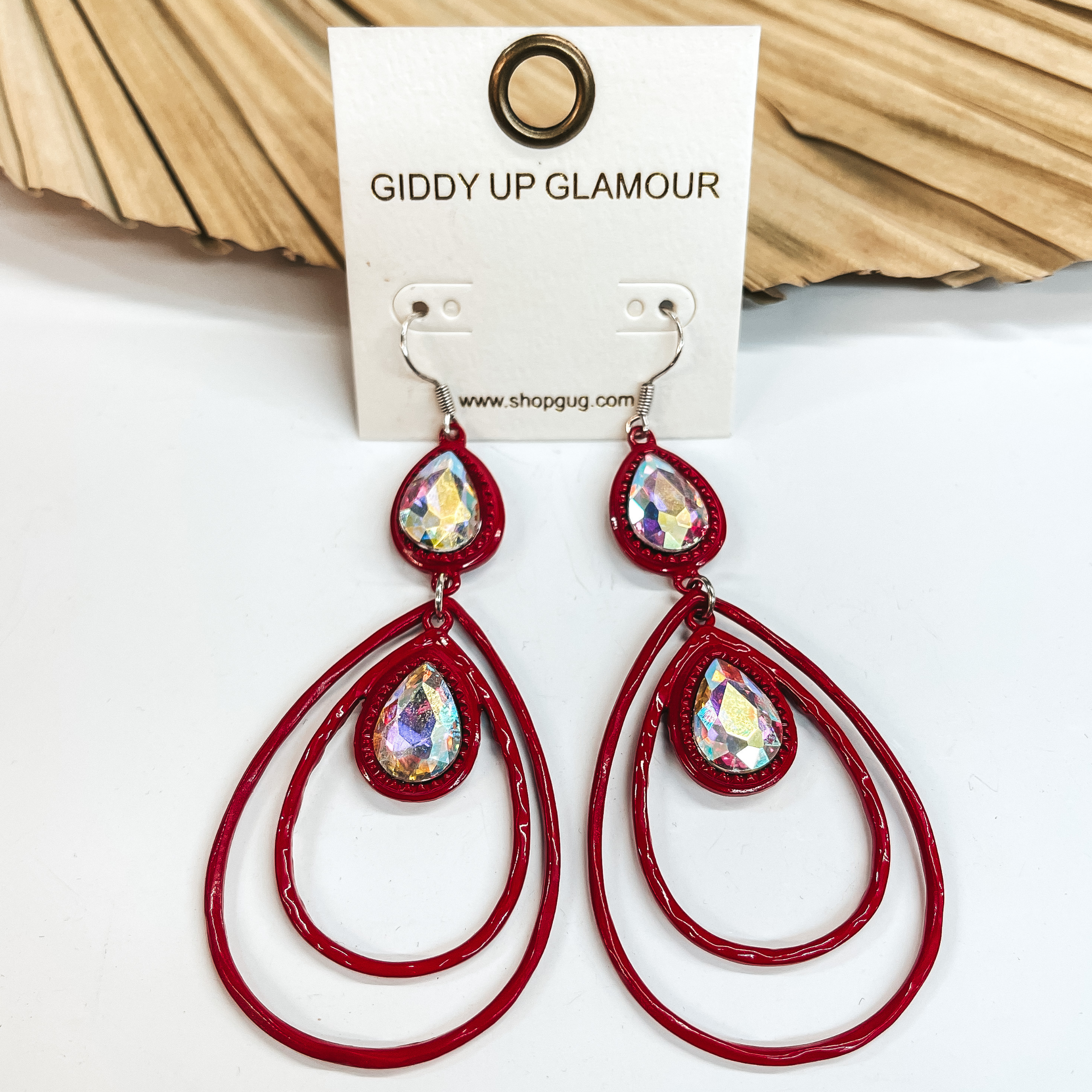 Red double teardrop earrings with two teardrop cut ab crystals. Teardrop cut ab crystal in a red setting then two red teardrops with another ab crystal inside. Taken on a white background and leaned up against a dried up palm leaf.