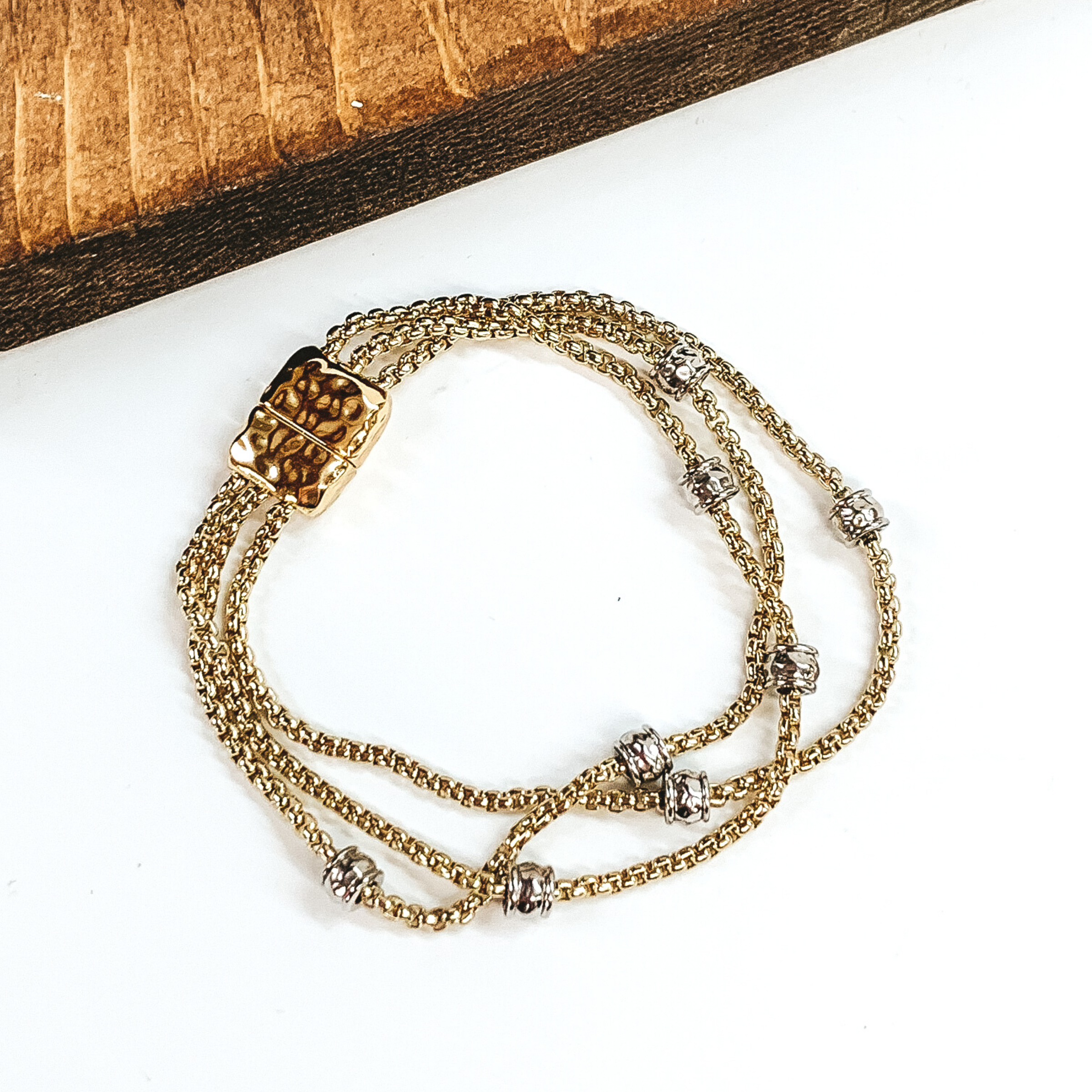 Gold, three stranded bracelet with silver spacers. This bracelet has a magnetic clasp. This bracelet is pictured on a white background.