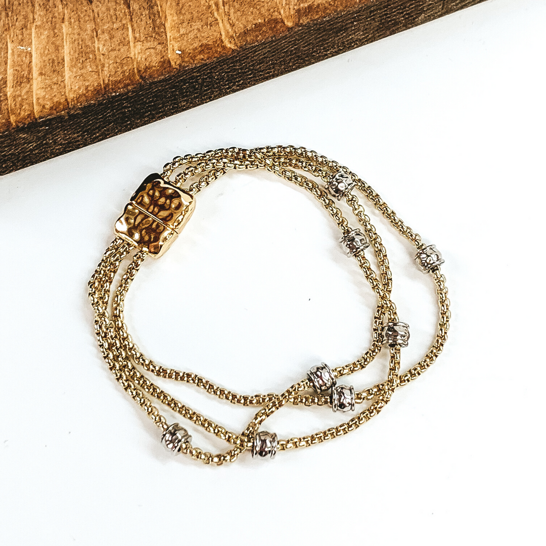 Gold, three stranded bracelet with silver spacers. This bracelet has a magnetic clasp. This bracelet is pictured on a white background.
