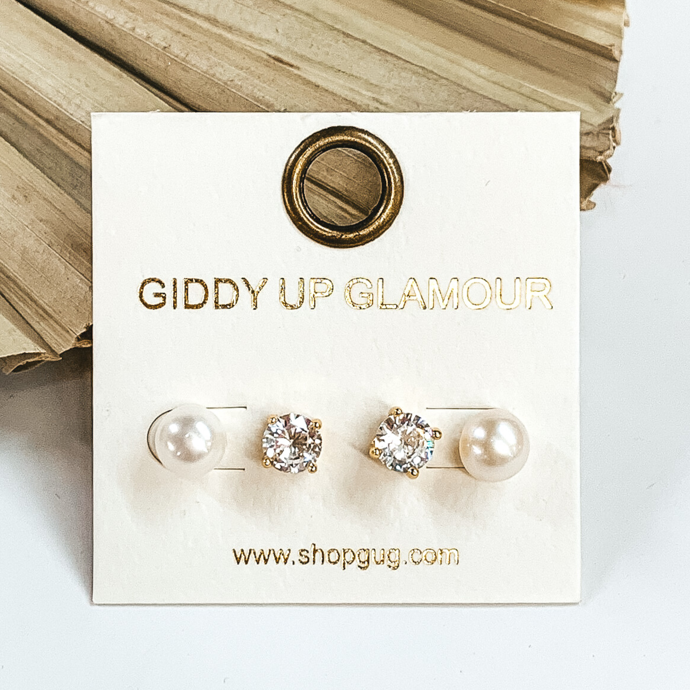 Clear crystal studs and white pearl studs. These earrings are pictured laying on a green palm leaf on a white background.
