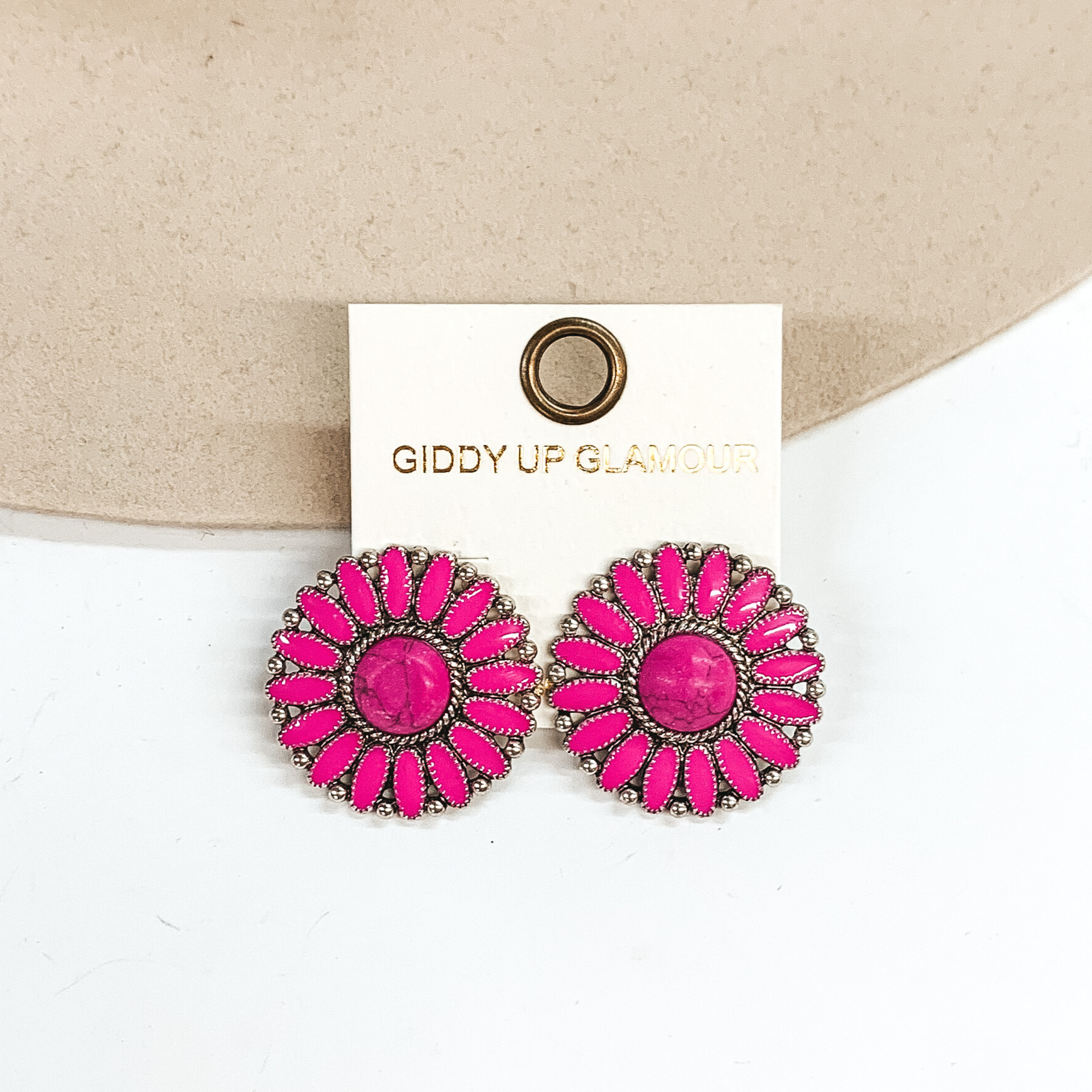 Pink concho earrings with a center pink stone and silver outline. These earrings are pictured on a white and ivory background. 