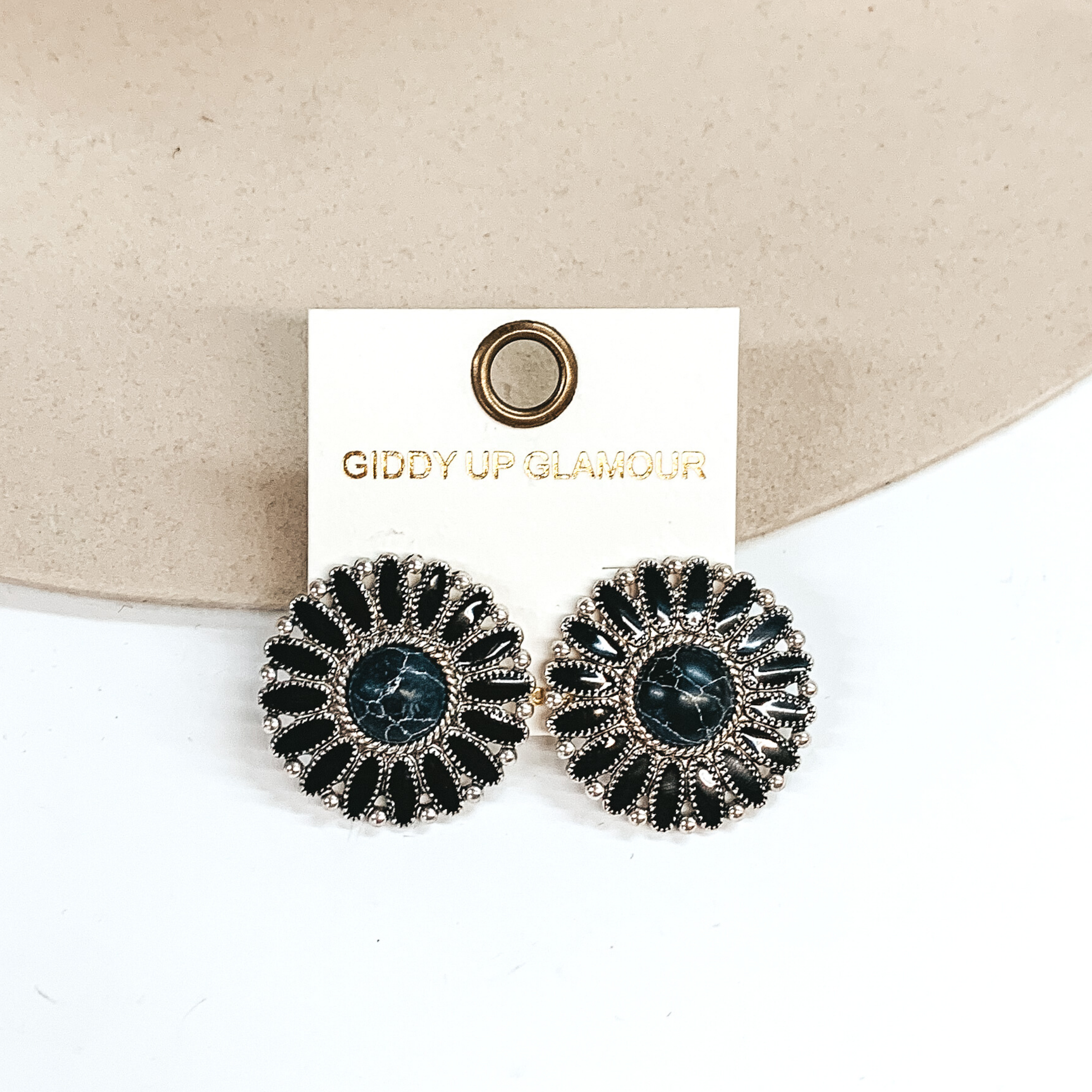 Black concho earrings with a center black stone and silver outline. These earrings are pictured on a white and ivory background.