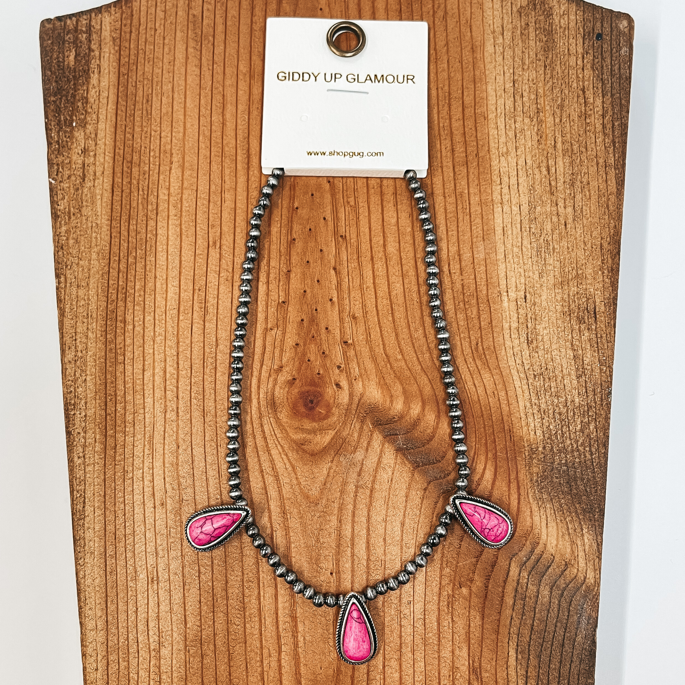 Faux navajo pearl choker with three teardrop shaped stones in pink with silver detailing around. Taken on a brown block and white background.