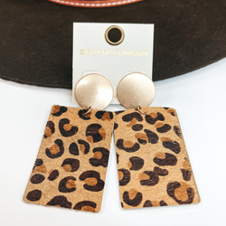 Gold circle stud earrings with leopard print on  leather hide. Taken on a white background and  leaned up against a dark brown hat.