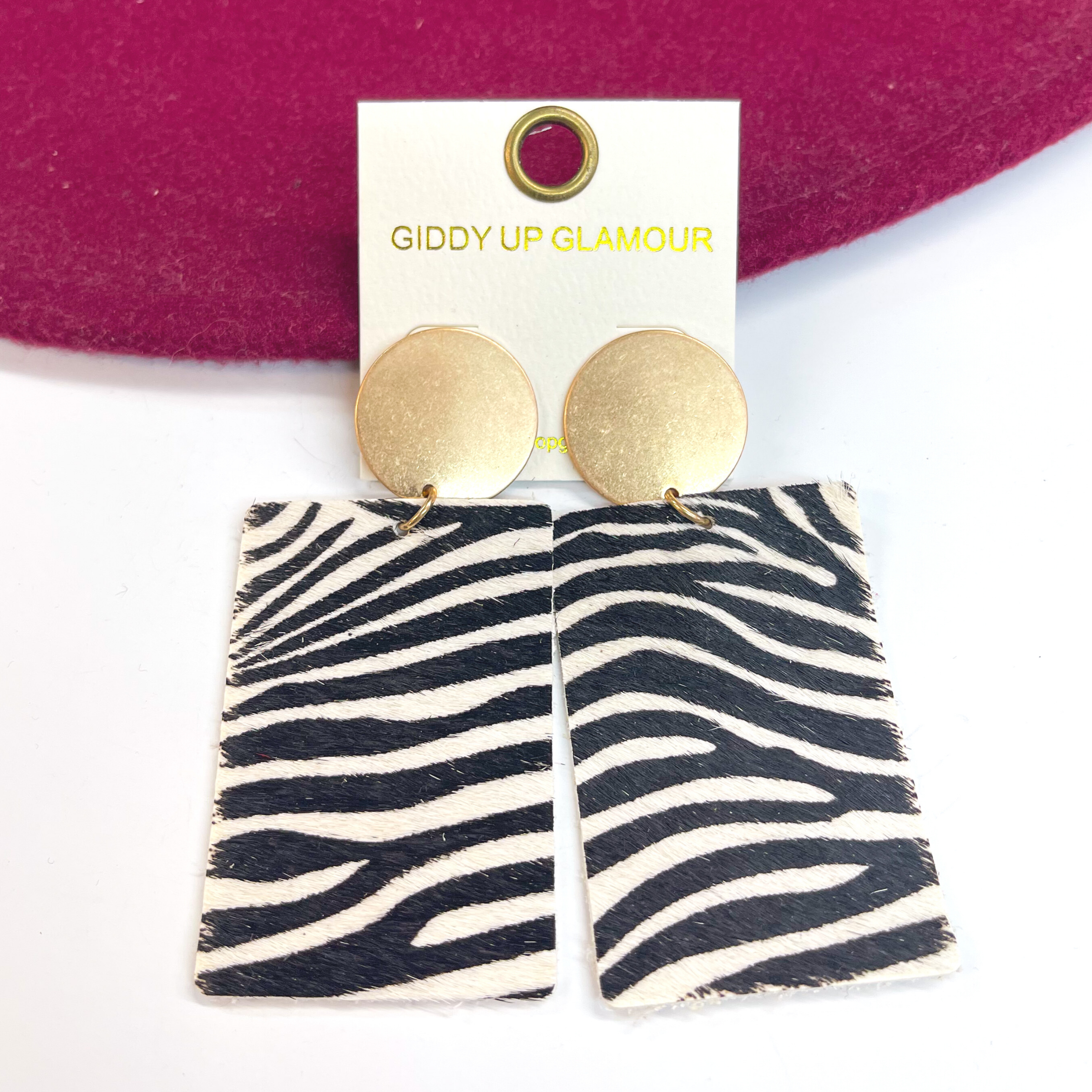 Gold circle stud earrings with zebra print on  leather hide. Taken on a white background and  leaned up against a burgundy hat.